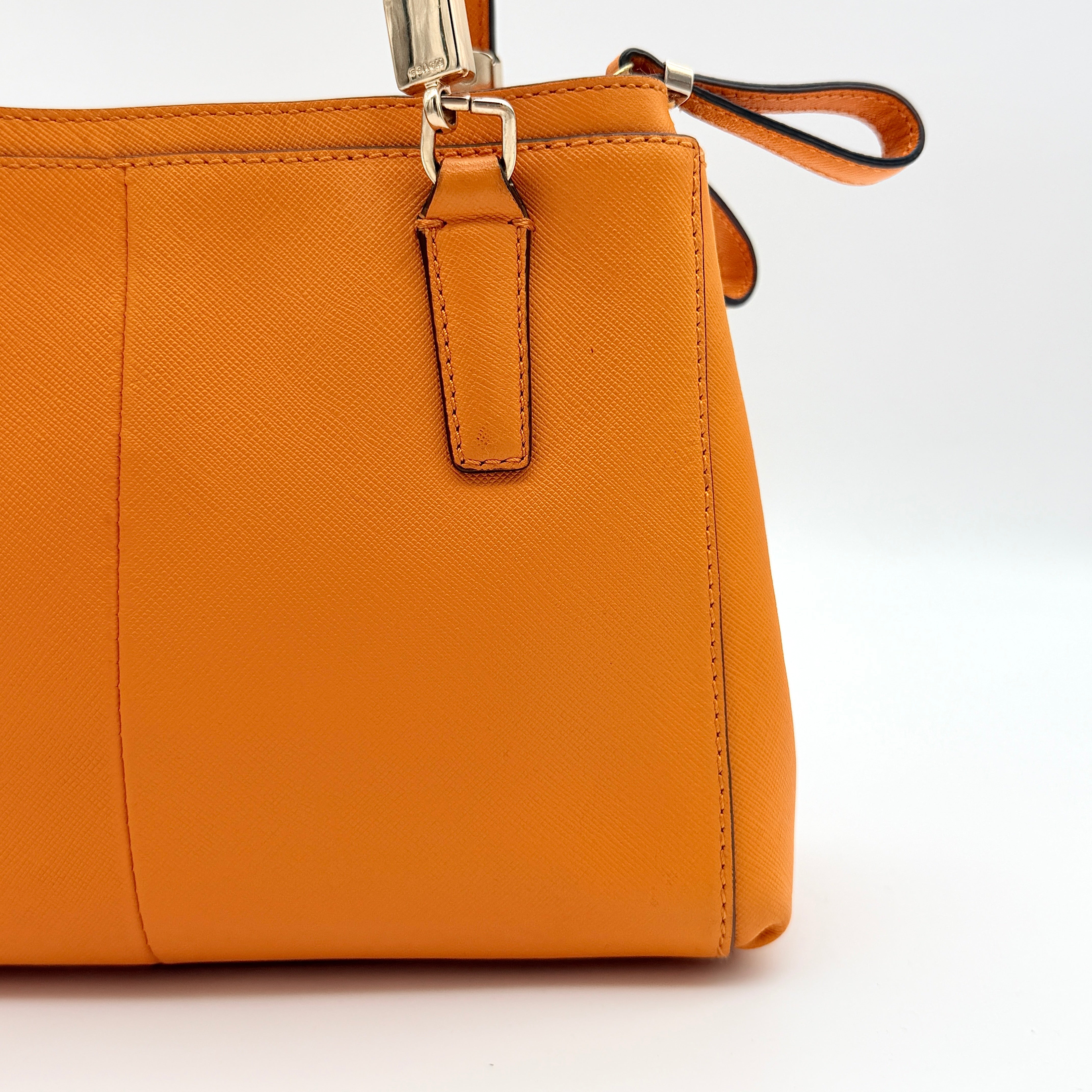 Coach Christie Carryall handbag in orange leather with gold hardware and structured handles, photographed on a white background.