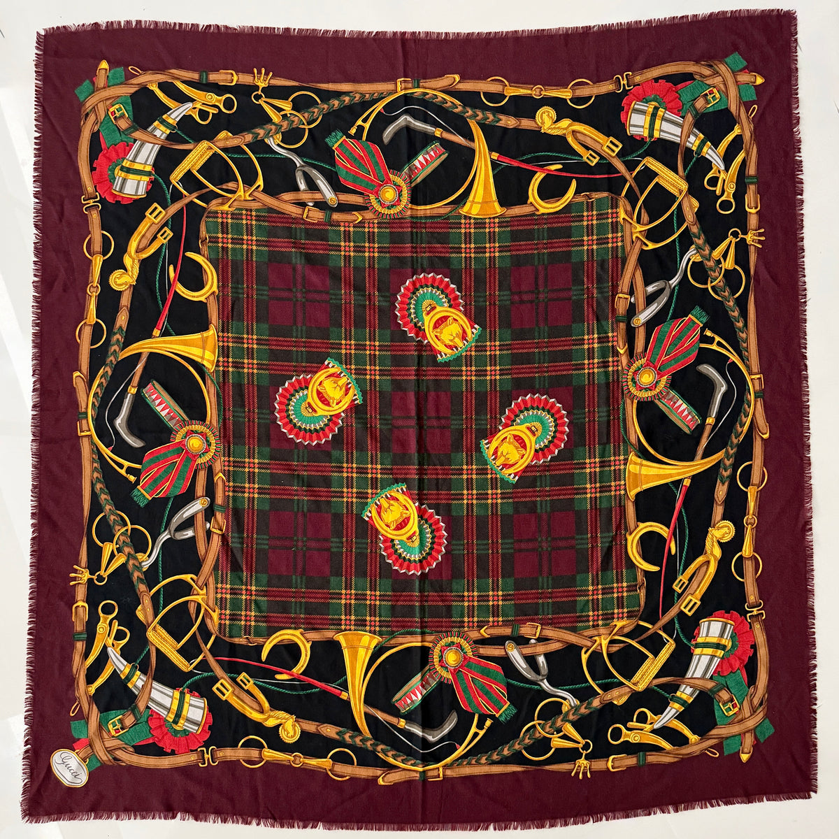 Gucci equestrian tartan shawl scarf in burgundy with heritage motifs and a fringed edge, styled folded.
