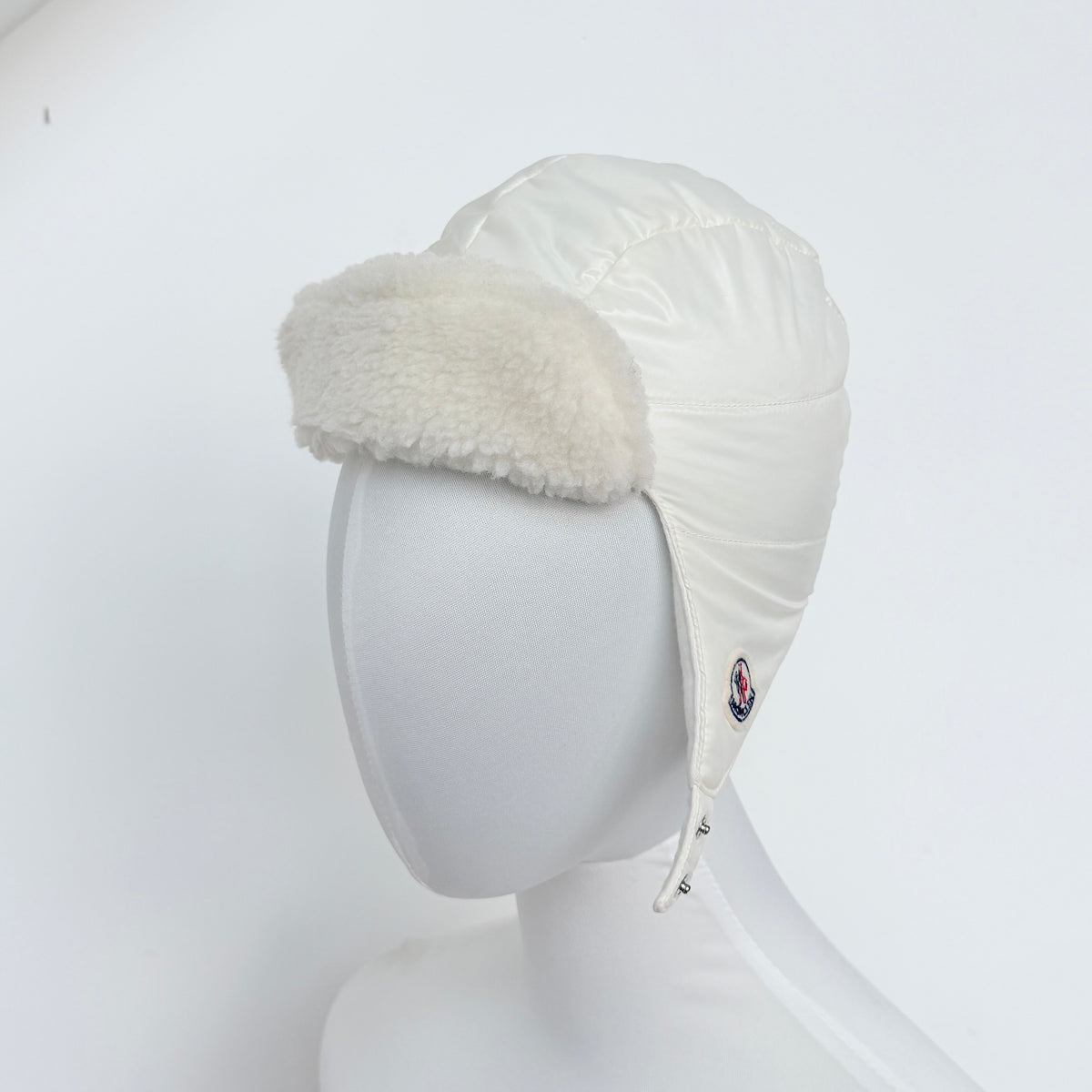 Moncler ivory quilted trapper hat with plush faux fur trim and signature logo patch displayed on white background.