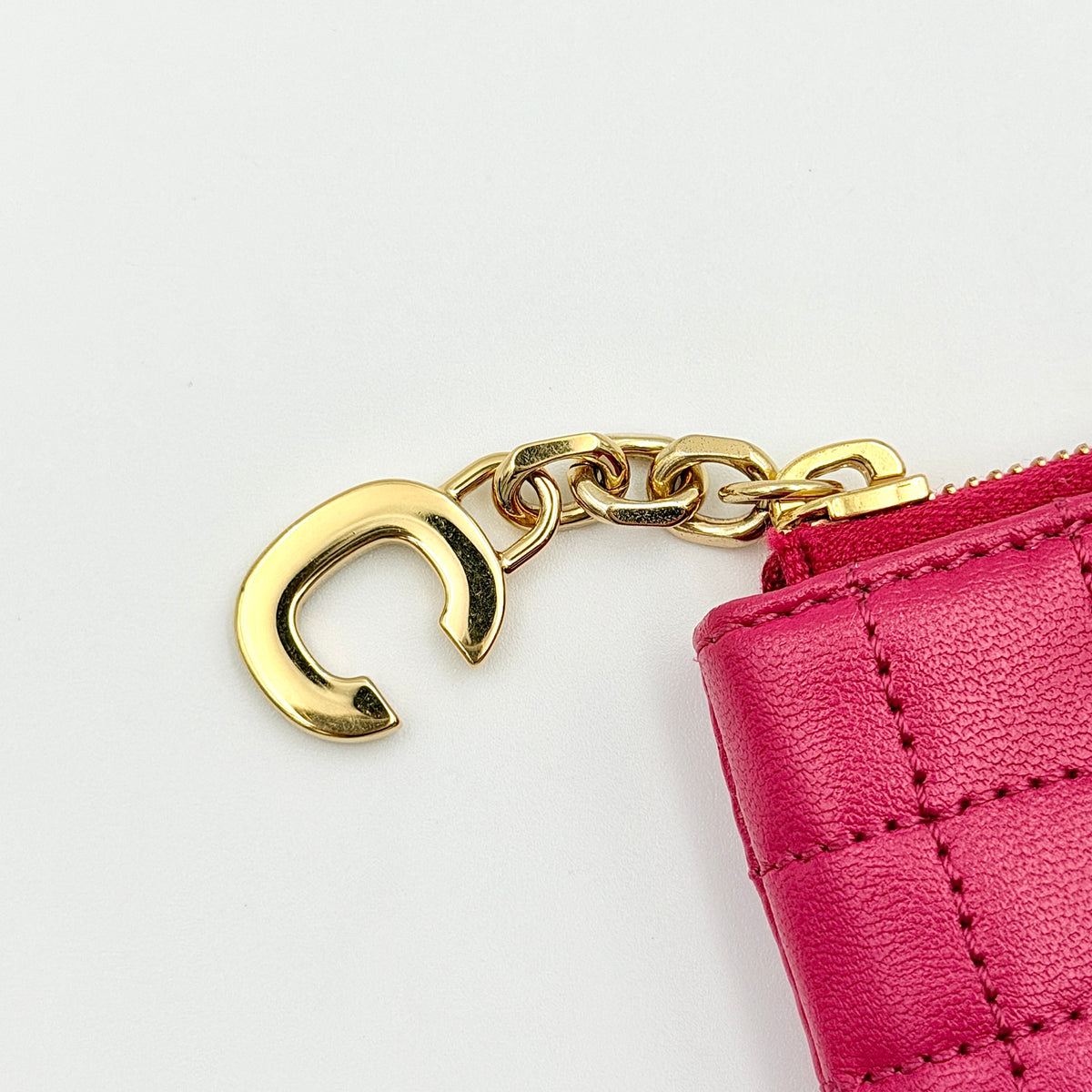 Celine quilted pink coin and card wallet with gold C charm, displayed on a black Celine dust bag.