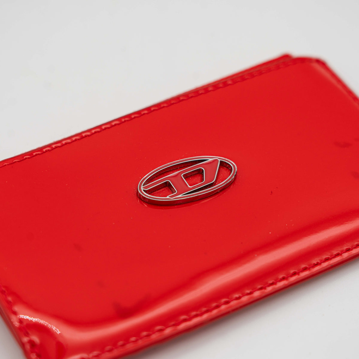 Diesel red patent card holder with silver logo plaque and top zip, set against a clean background.