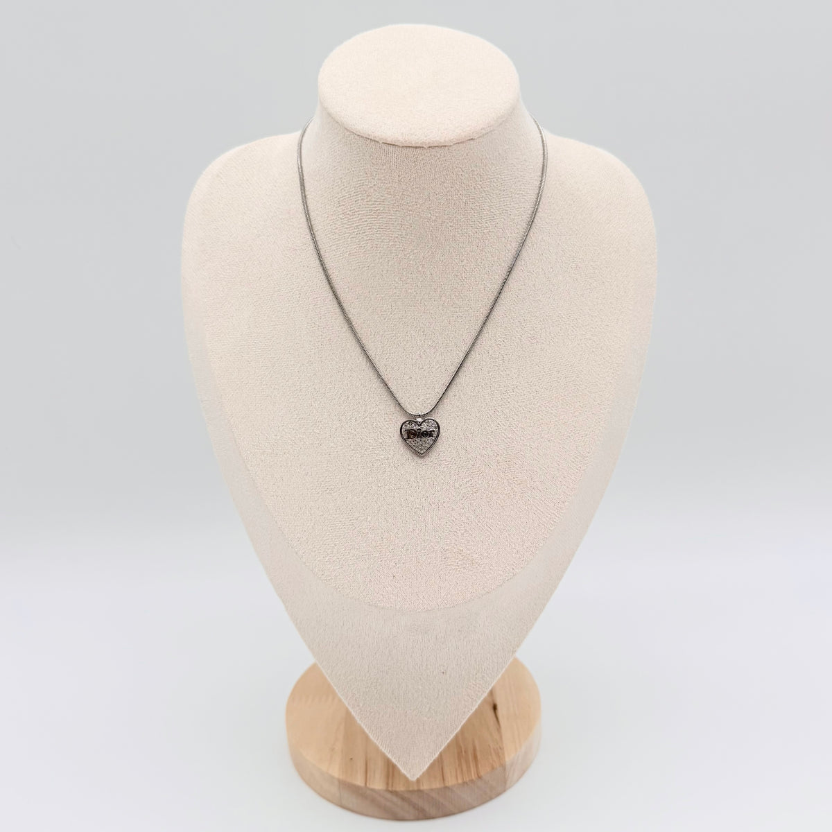 Dior silver necklace with a rhinestone heart pendant and Dior logo, laid flat with CD tag visible.