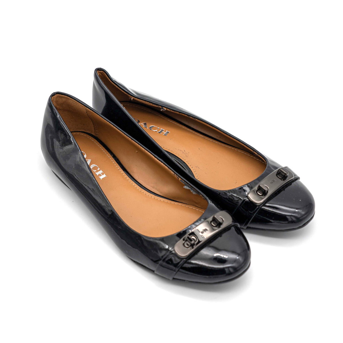 Coach Oswald Turnlock black patent leather ballet flats with dark metal hardware on the toe, photographed on a white background.