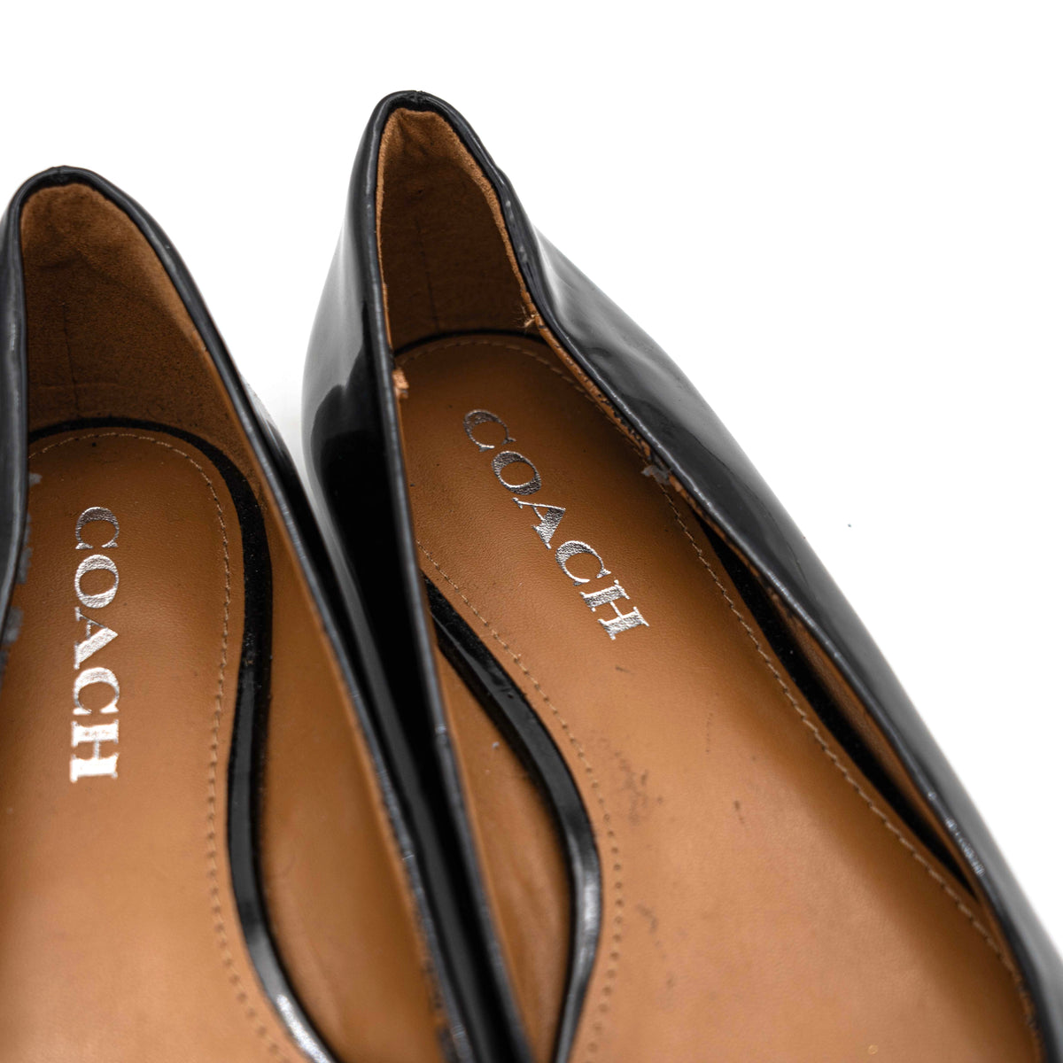 Coach Oswald Turnlock black patent leather ballet flats with dark metal hardware on the toe, photographed on a white background.