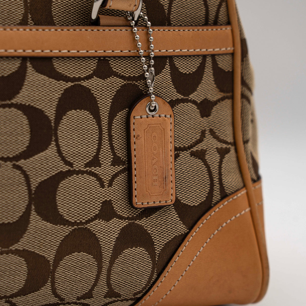 Coach Signature Hampton Satchel Boston Bag in beige and tan canvas with leather trim and silver hardware, styled on a clean background.