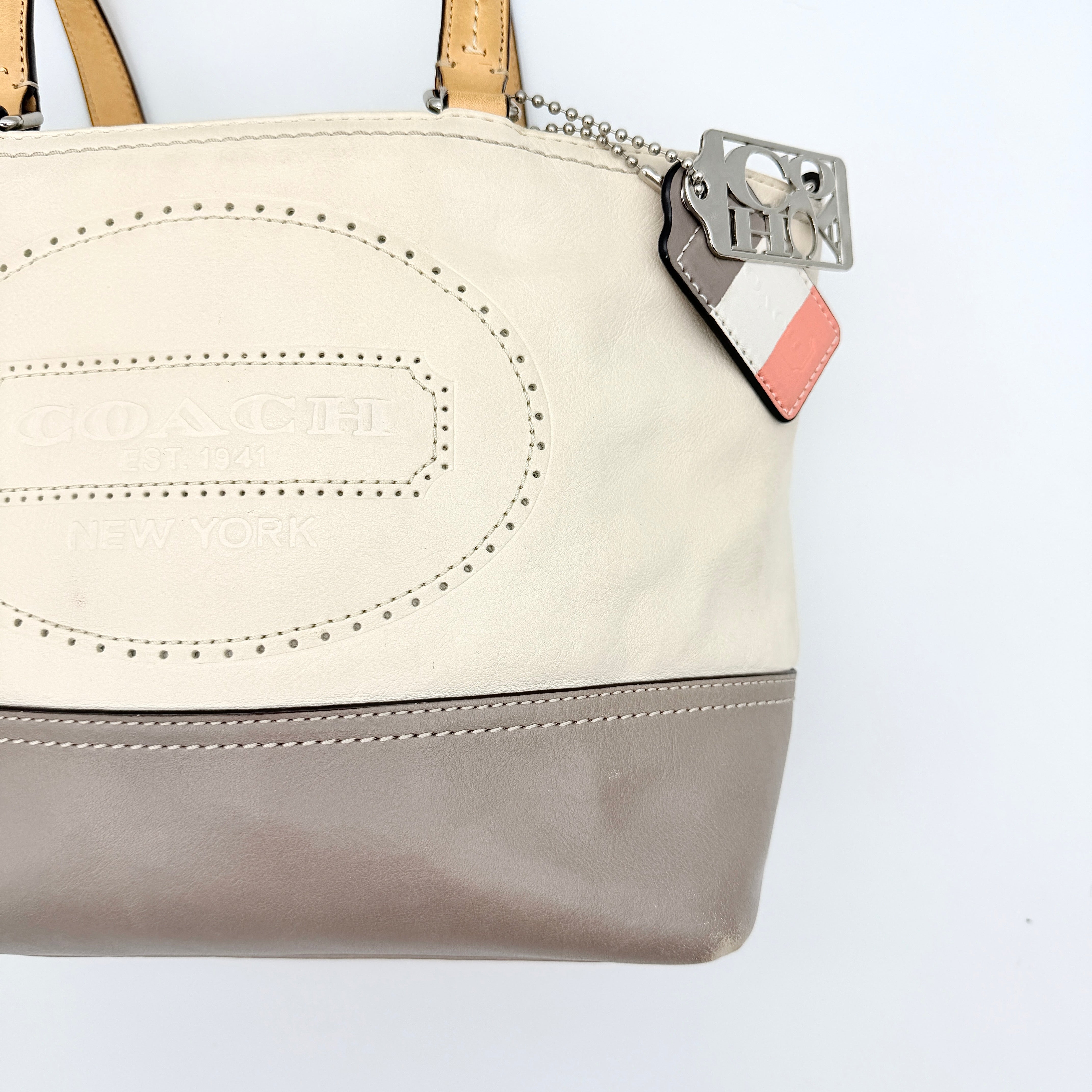 Coach Hampton Weekend perforated cream and grey leather tote bag with tan handles and a silver Coach charm, displayed against a white background.