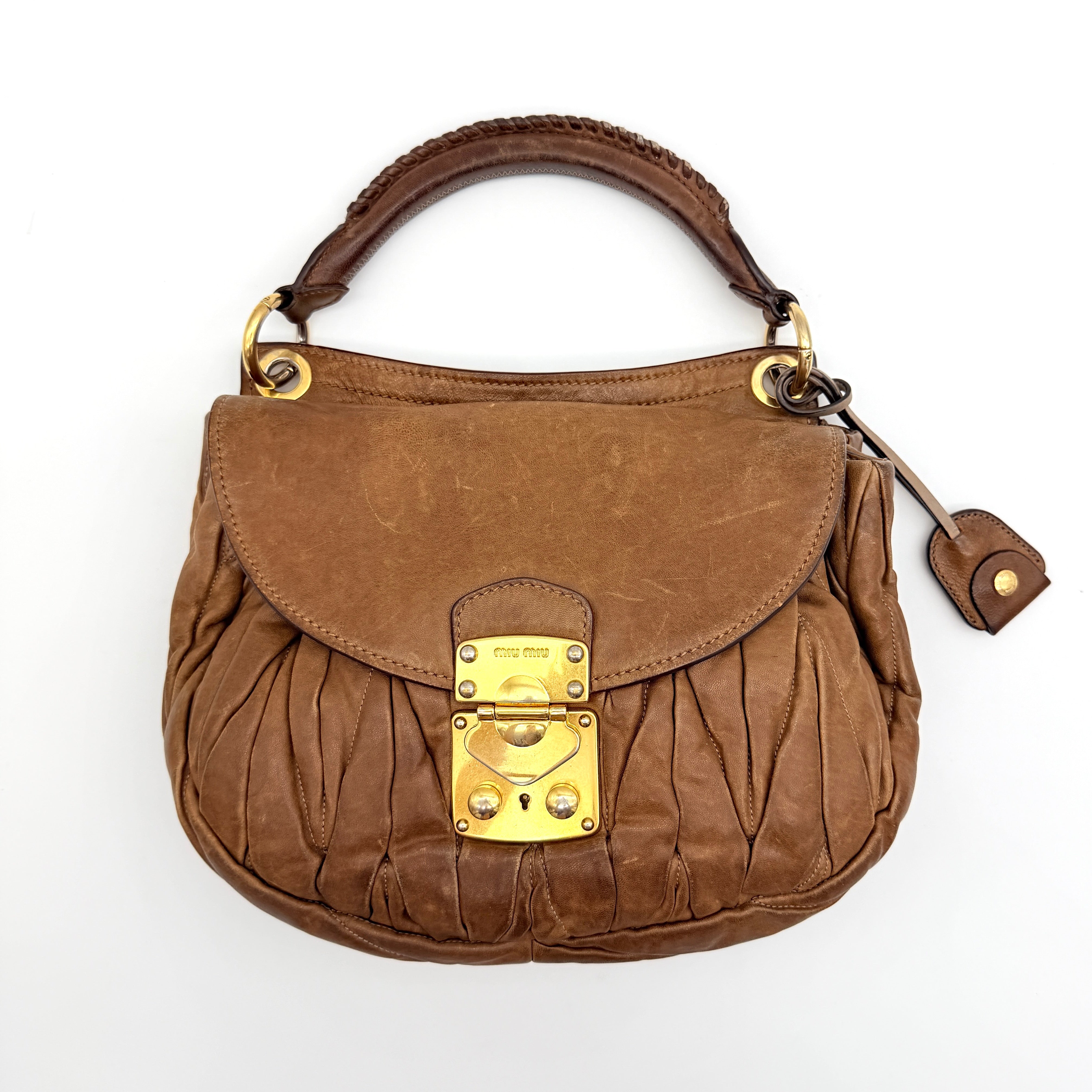 Miu Miu brown Matelasse Coffer Hobo bag with gold hardware, detachable strap, and dust bag displayed on a flat surface.