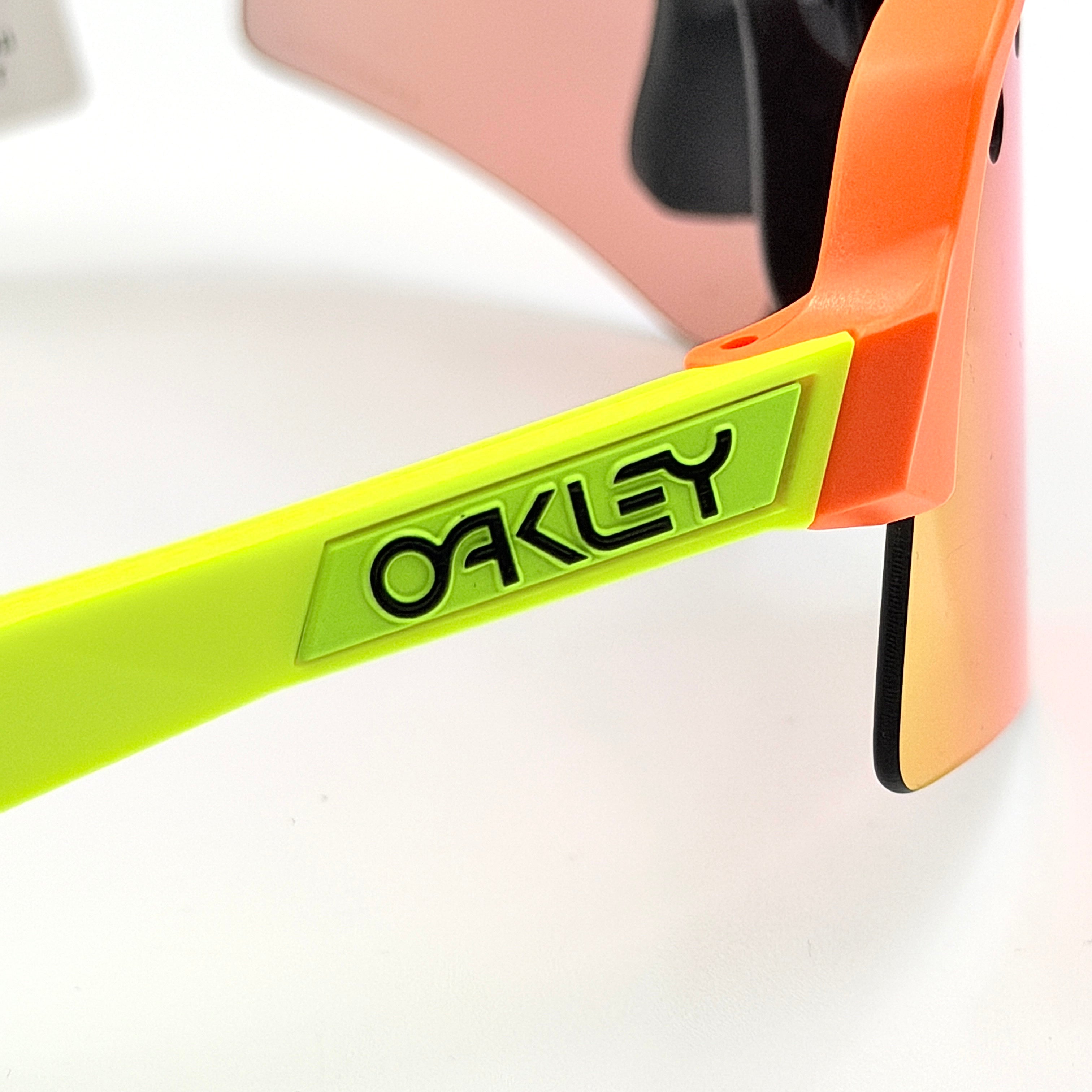 Oakley Sutro Lite Sweep sunglasses in neon yellow and orange with Prizm Trail Torch shield lens, displayed with box and case.