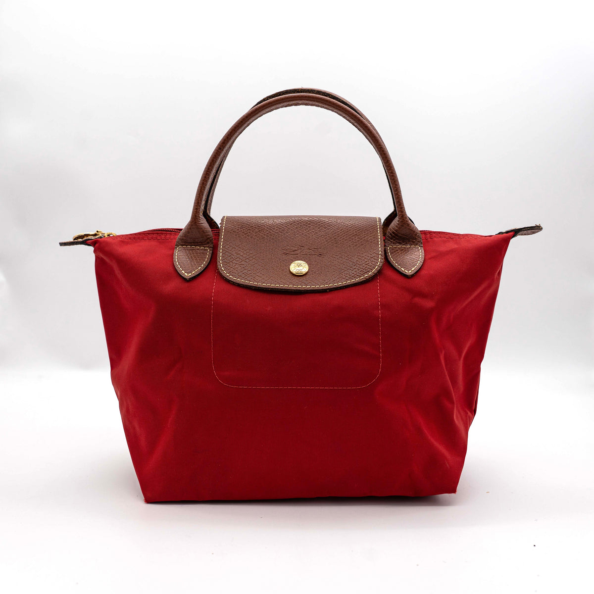 Longchamp Le Pliage handbag in red nylon with brown leather handles and gold-tone accents, photographed on a white background.