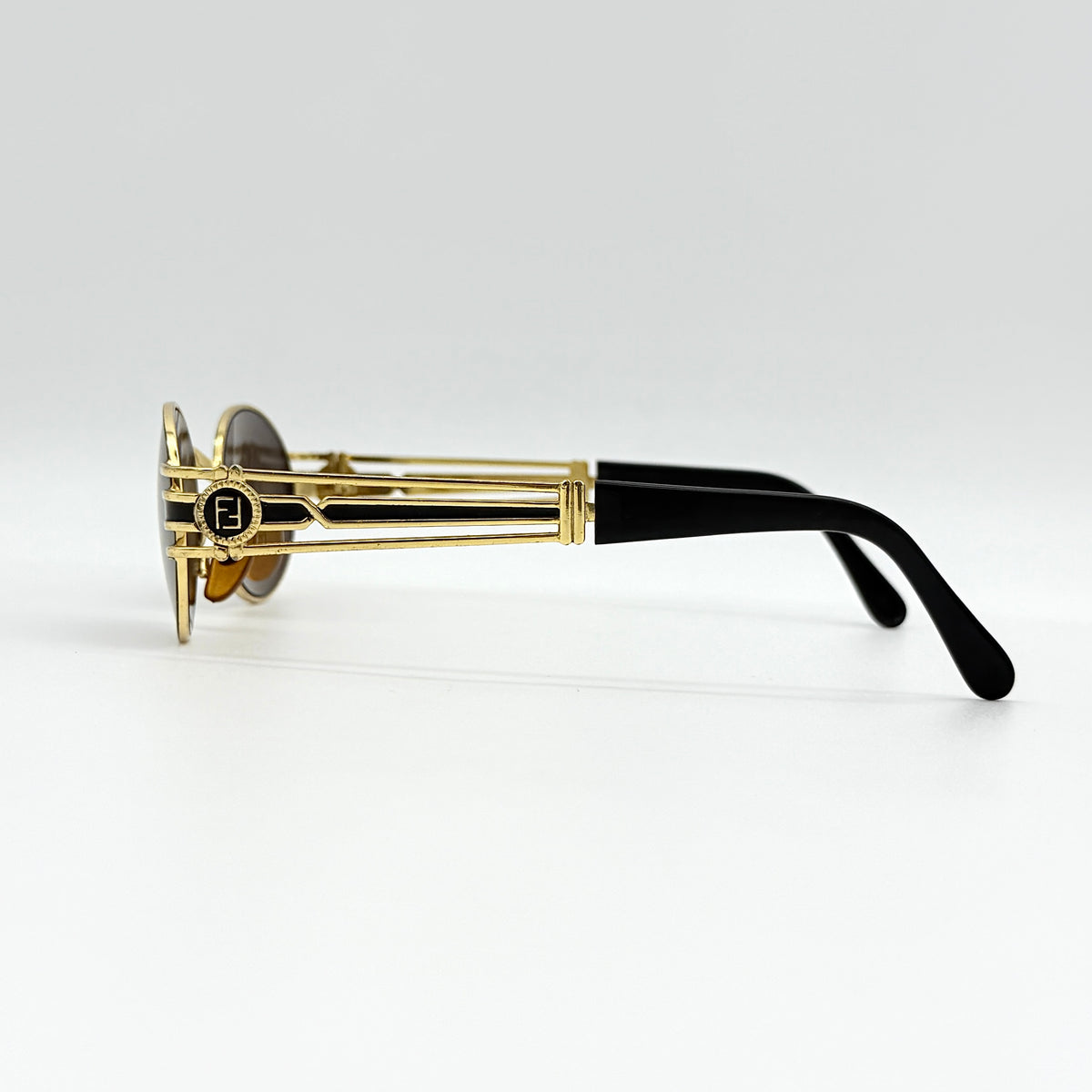 Fendi FF SL7031 oval sunglasses with gold-tone frame, brown lenses, and black arms, shown at an angled side view.