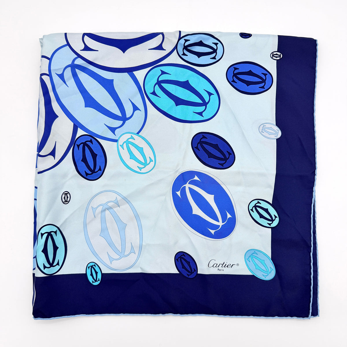Cartier silk scarf in blue and white with graphic monogram logo print and navy border, elegantly arranged.