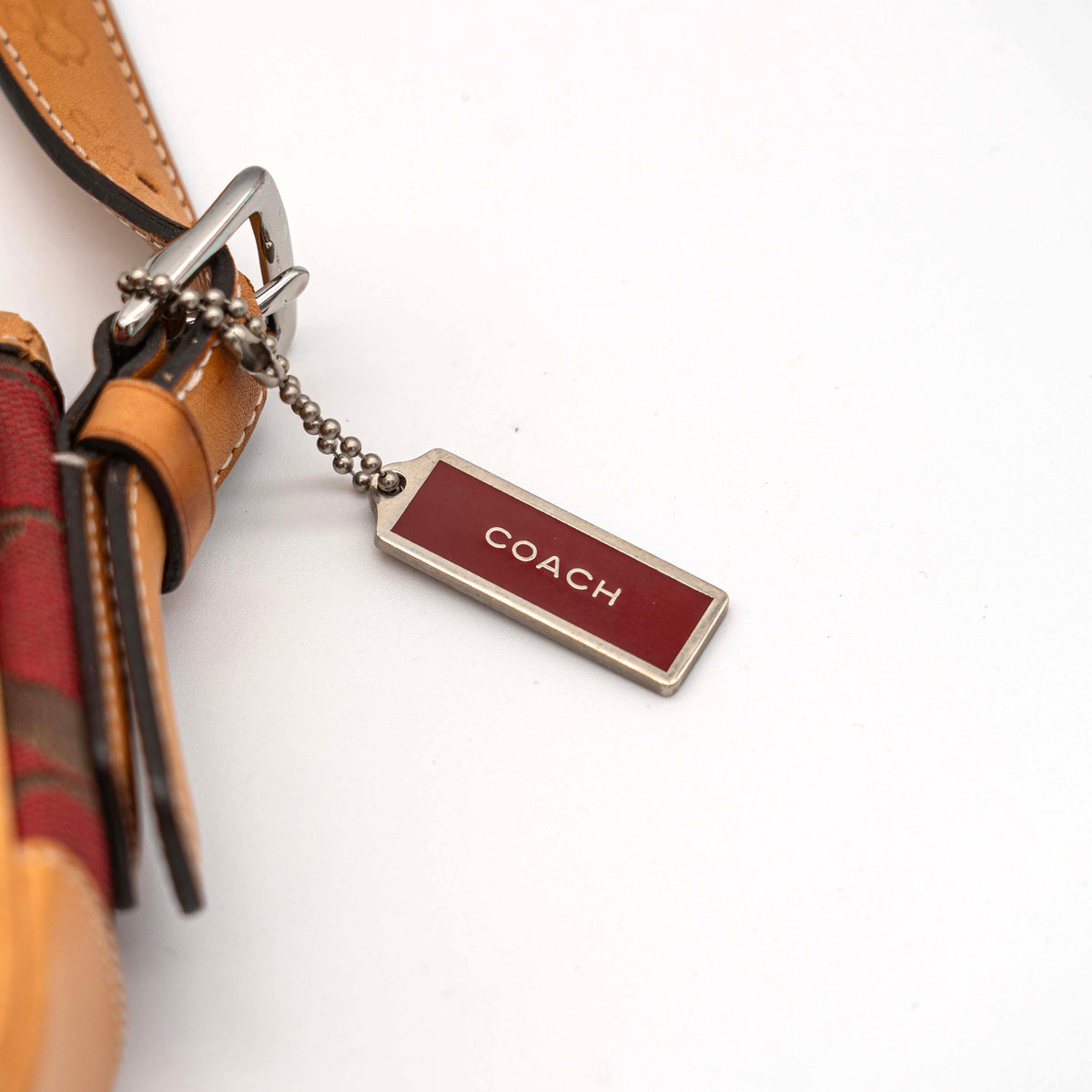 Coach Signature Soho Buckle Baguette in red and tan canvas with leather trim and a silver buckle, shown on a white background.