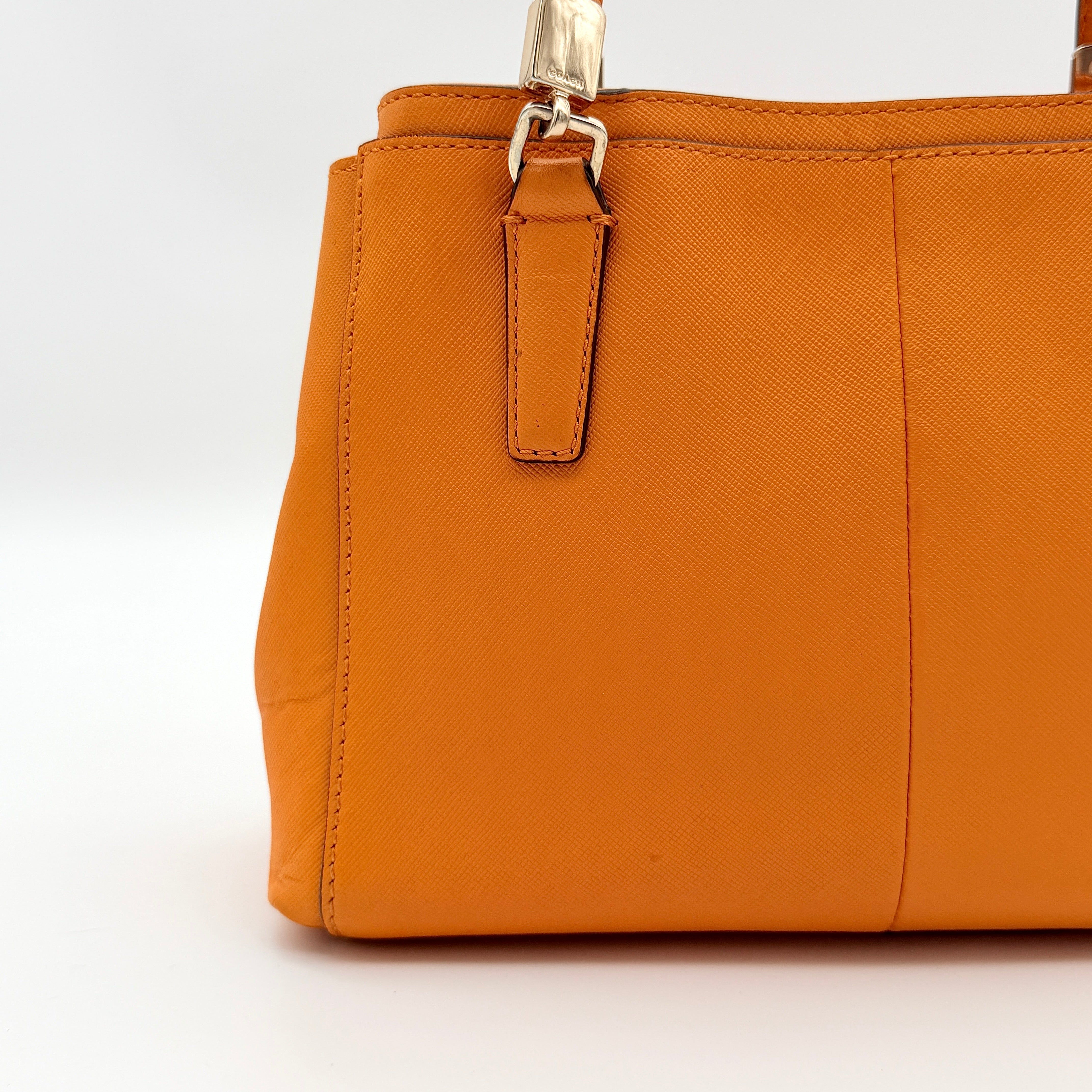 Coach Christie Carryall handbag in orange leather with gold hardware and structured handles, photographed on a white background.