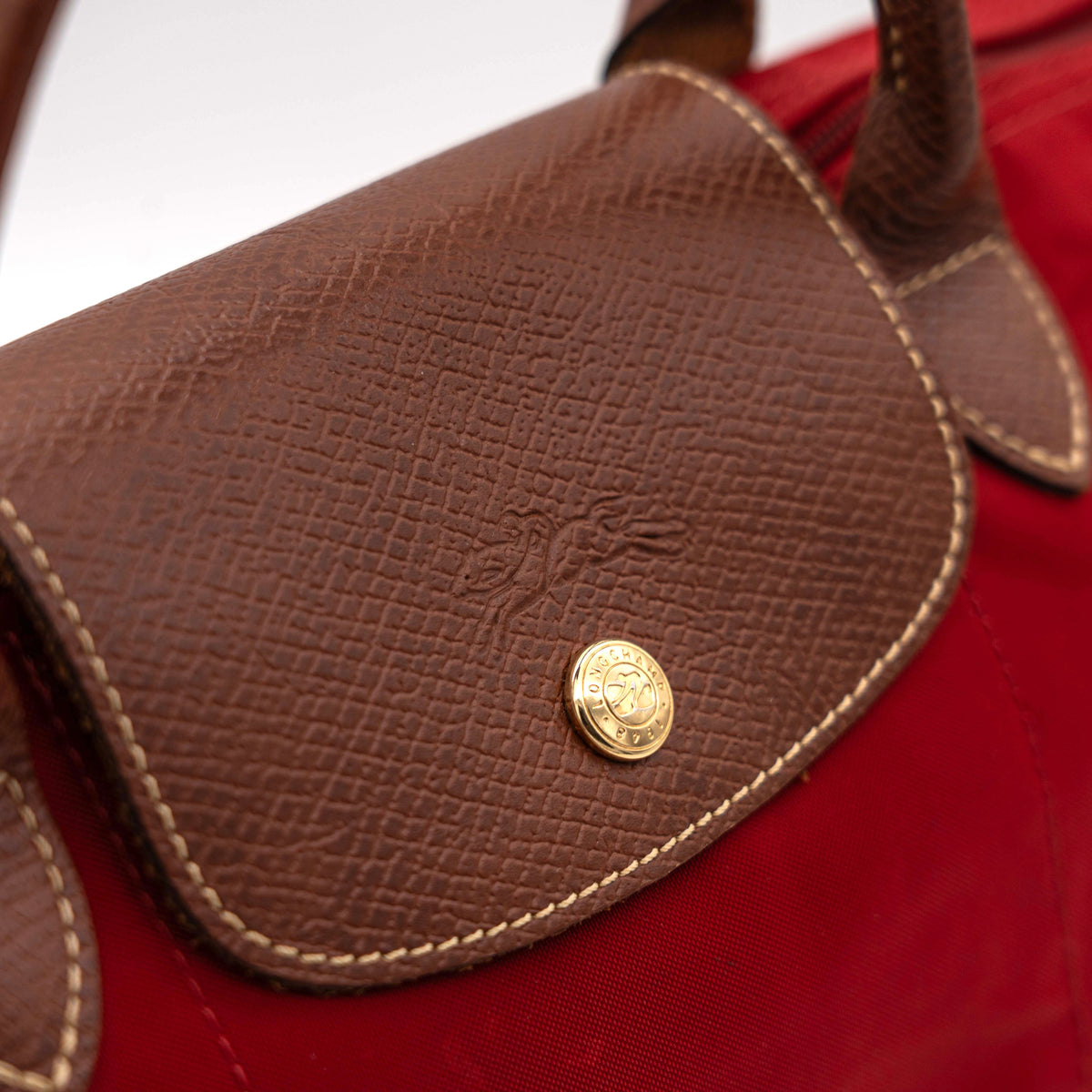 Longchamp Le Pliage handbag in red nylon with brown leather handles and gold-tone accents, photographed on a white background.