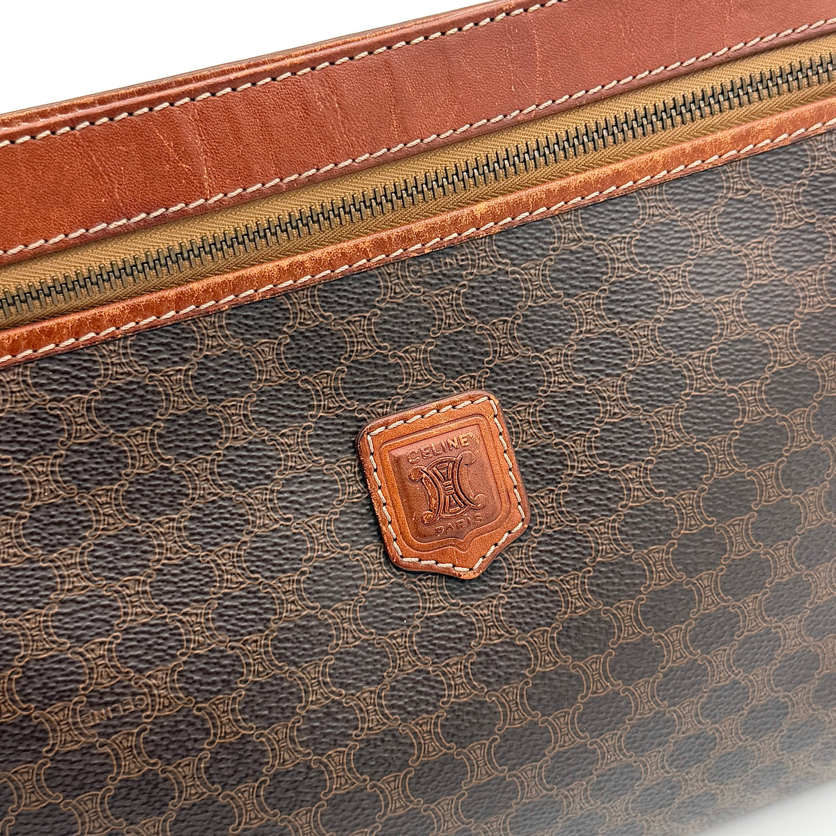 Celine Triomphe Macadam clutch bag in brown canvas with tan leather trim and gold hardware, shown with wrist strap.