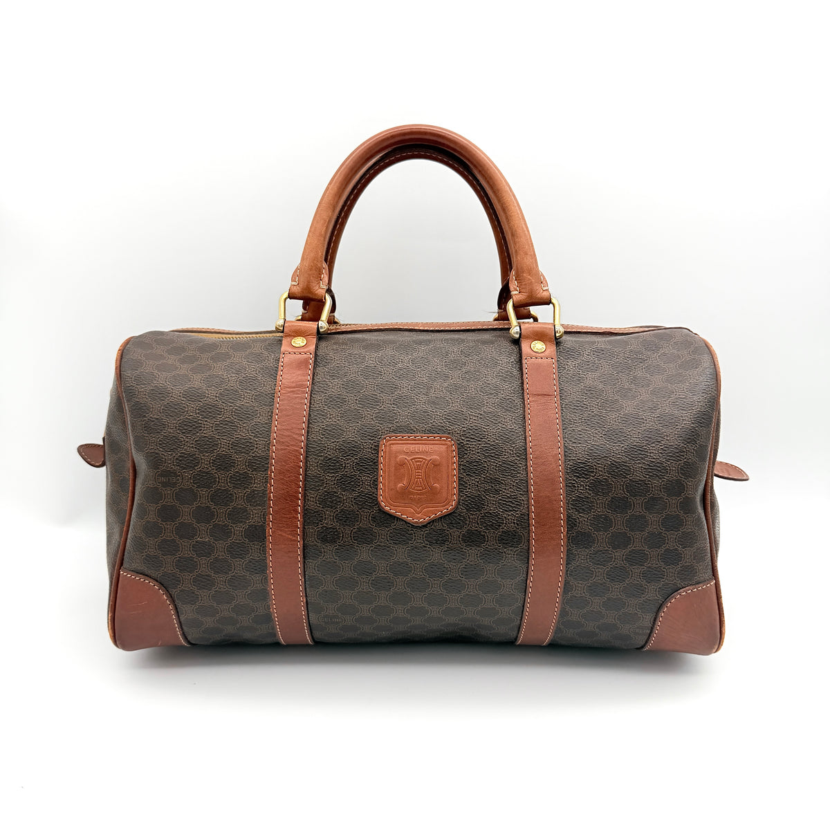 Celine Macadam Triomphe Boston Bag in brown coated canvas with tan leather and gold-tone hardware, shown against a white background.