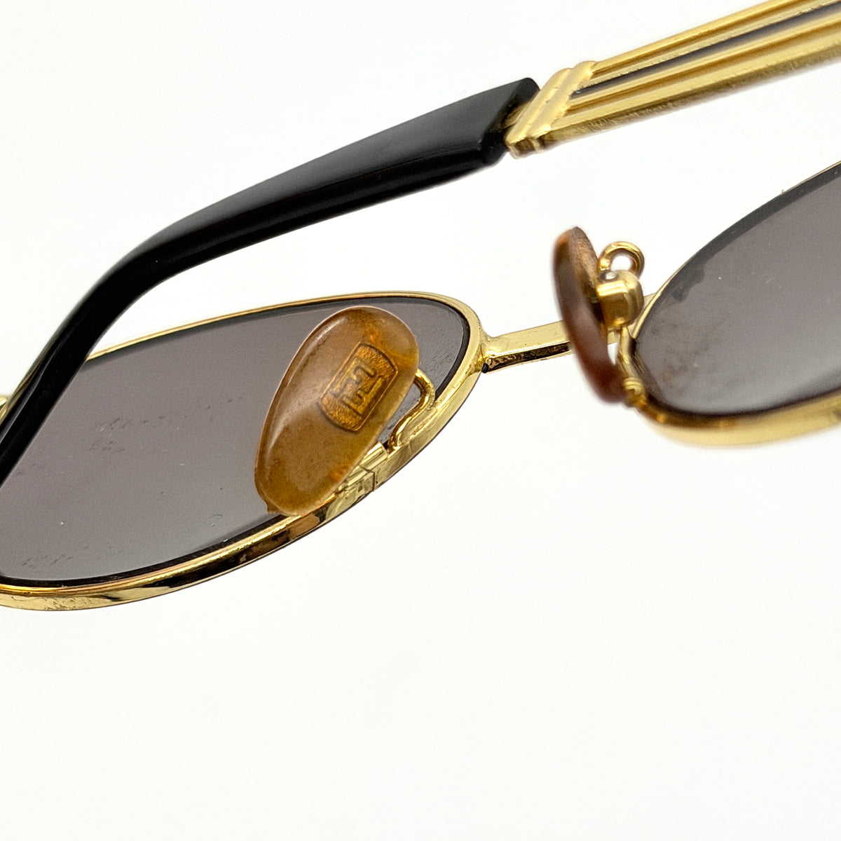 Fendi FF SL7031 oval sunglasses with gold-tone frame, brown lenses, and black arms, shown at an angled side view.