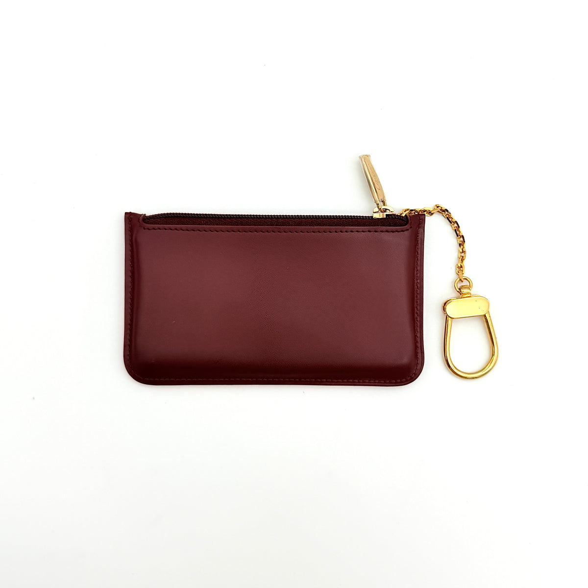 Cartier Must de Cartier burgundy leather coin purse with gold chain key holder and embossed logo, photographed on white.