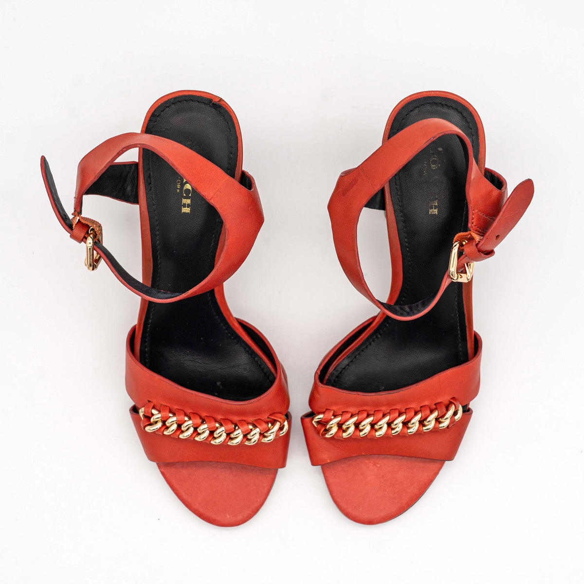 Coach Phoebe block heels in red leather with gold chain detailing, displayed with chunky wood-stacked heels and adjustable ankle straps.