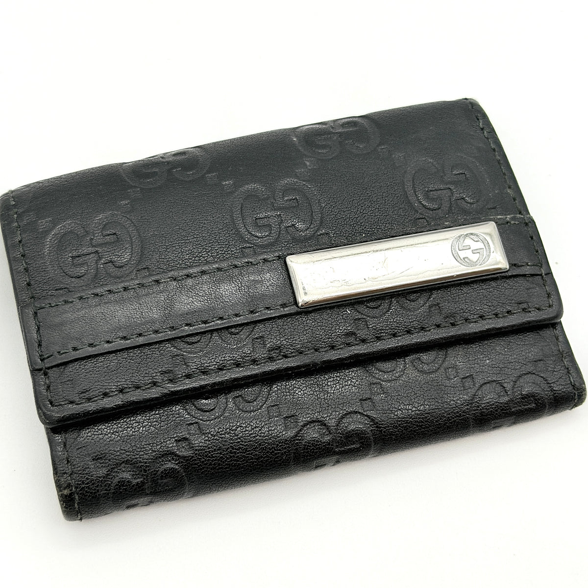 Gucci Guccissima GG Monogram black leather key case with silver-tone hardware, shown closed against a white background.