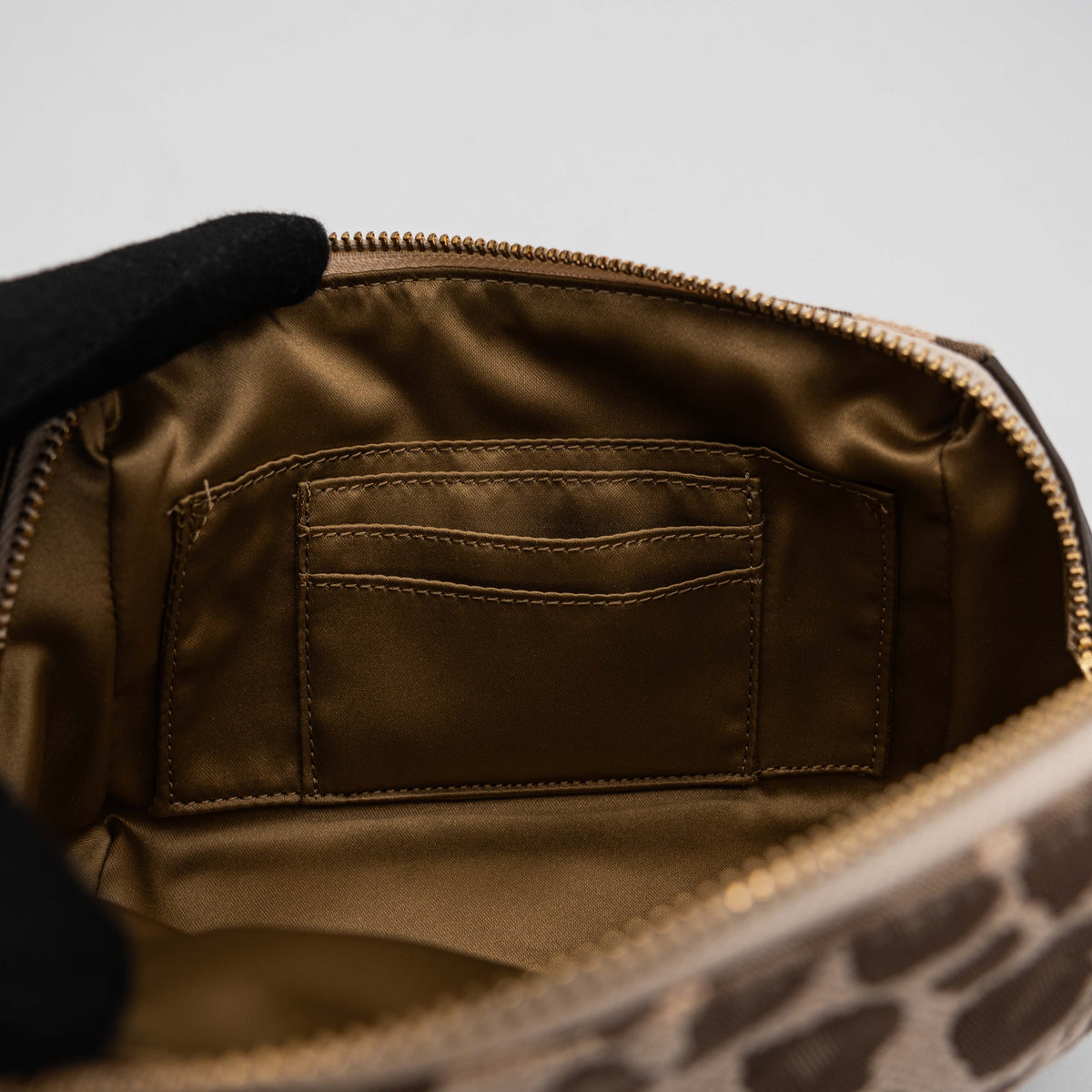 Coach cosmetic pouch in brown and beige leopard print canvas with chocolate leather trim and gold hardware, shown with wrist strap.