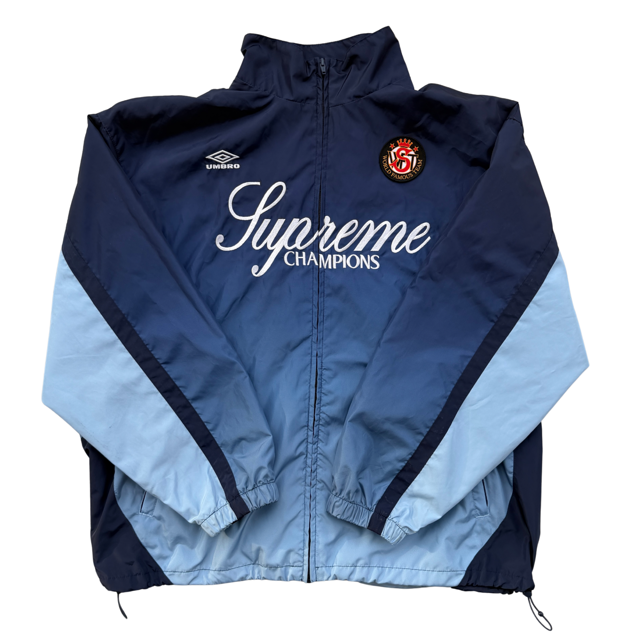 Supreme x Umbro blue gradient track jacket with white Supreme Champions lettering and crest, shown zipped with elastic cuffs and hem.