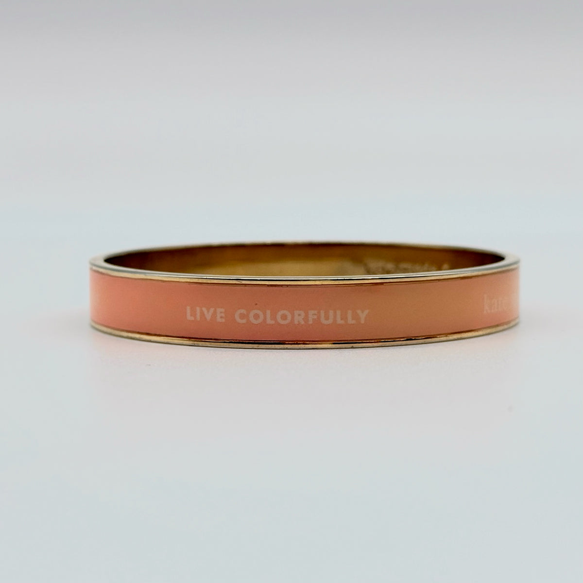 Kate Spade New York enamel bangle in orange with gold-tone interior and logo detailing, photographed on a white background.
