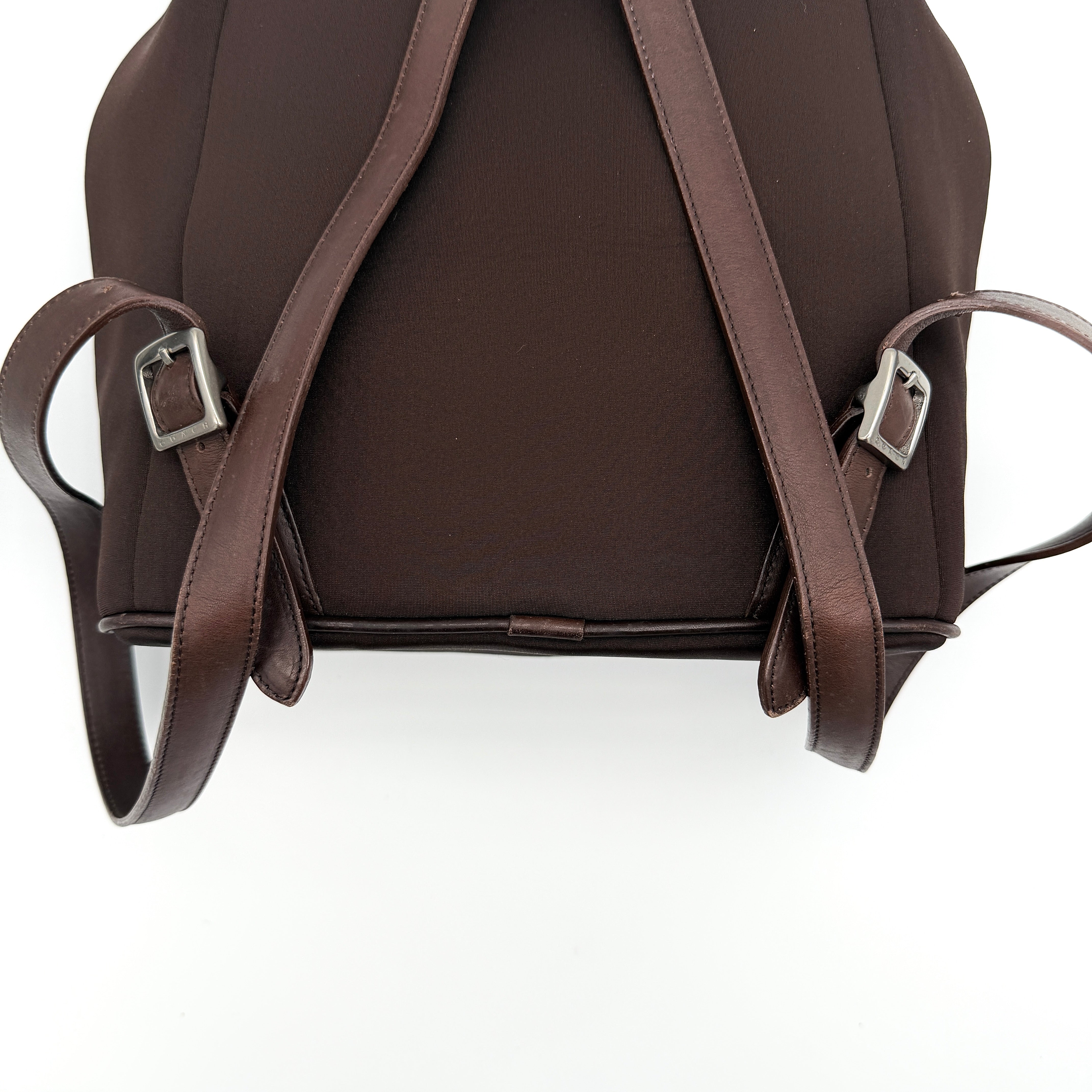 Coach brown neoprene drawstring backpack with leather trim, silver-tone hardware, and adjustable straps shown against a white background.
