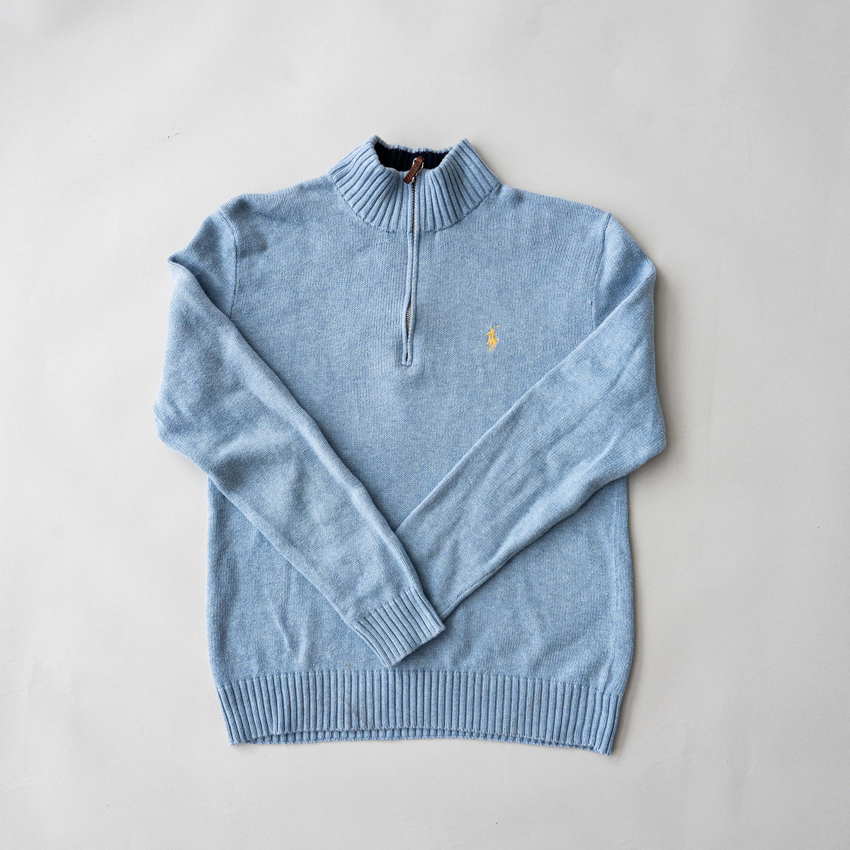 Polo Ralph Lauren light blue quarter zip mockneck cotton sweater laid flat with visible yellow pony logo.