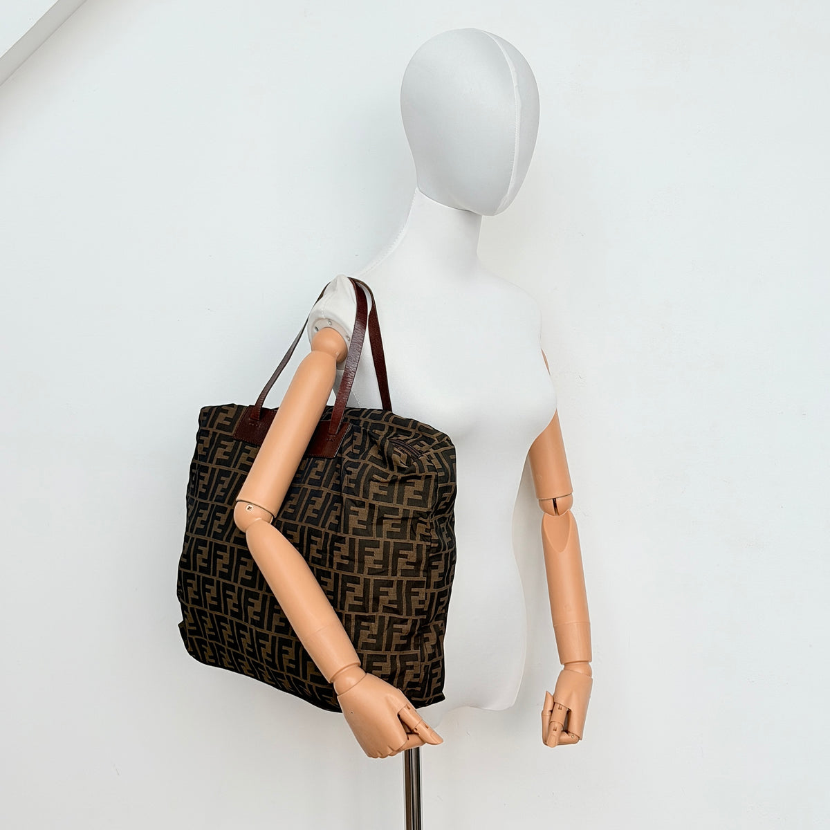 Fendi FF Zucca foldable tote bag in brown canvas with leather top handles and all-over monogram, shown standing upright.