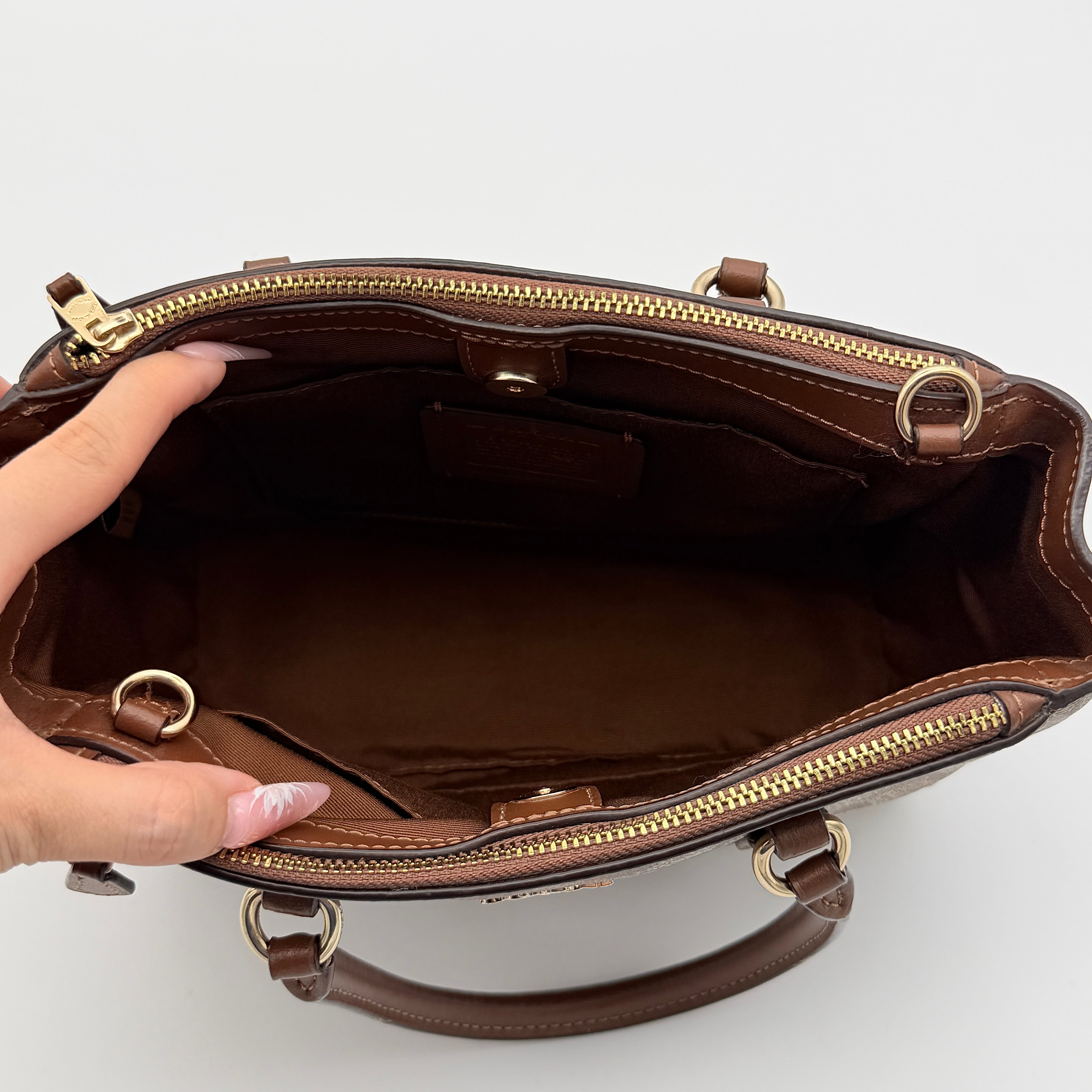 Coach Christie Carryall in beige and brown canvas with gold hardware and detachable strap, photographed in a studio setting.
