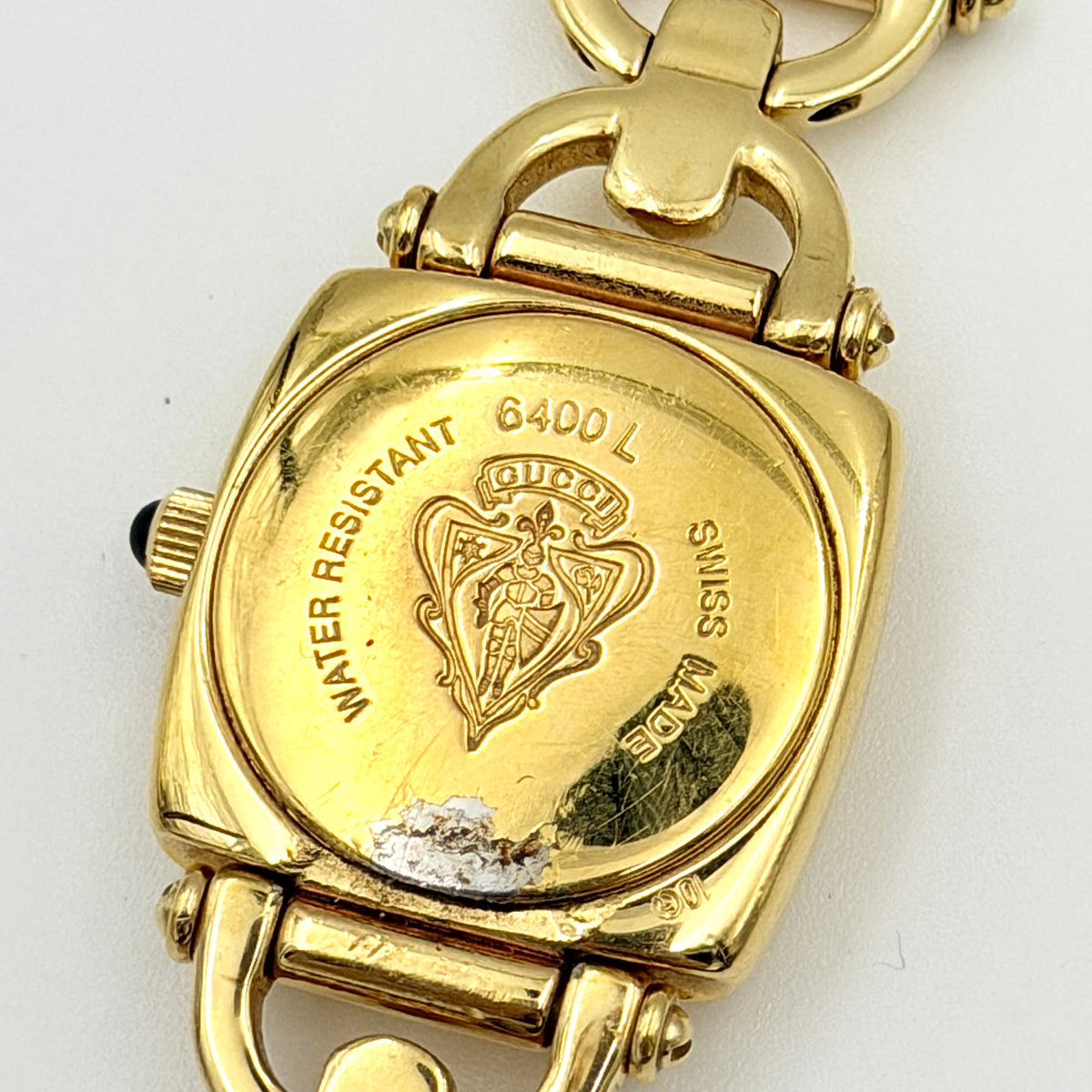 Gucci 6400L gold-tone bracelet watch with a black dial and distinctive horsebit links, showcased on a clear stand.