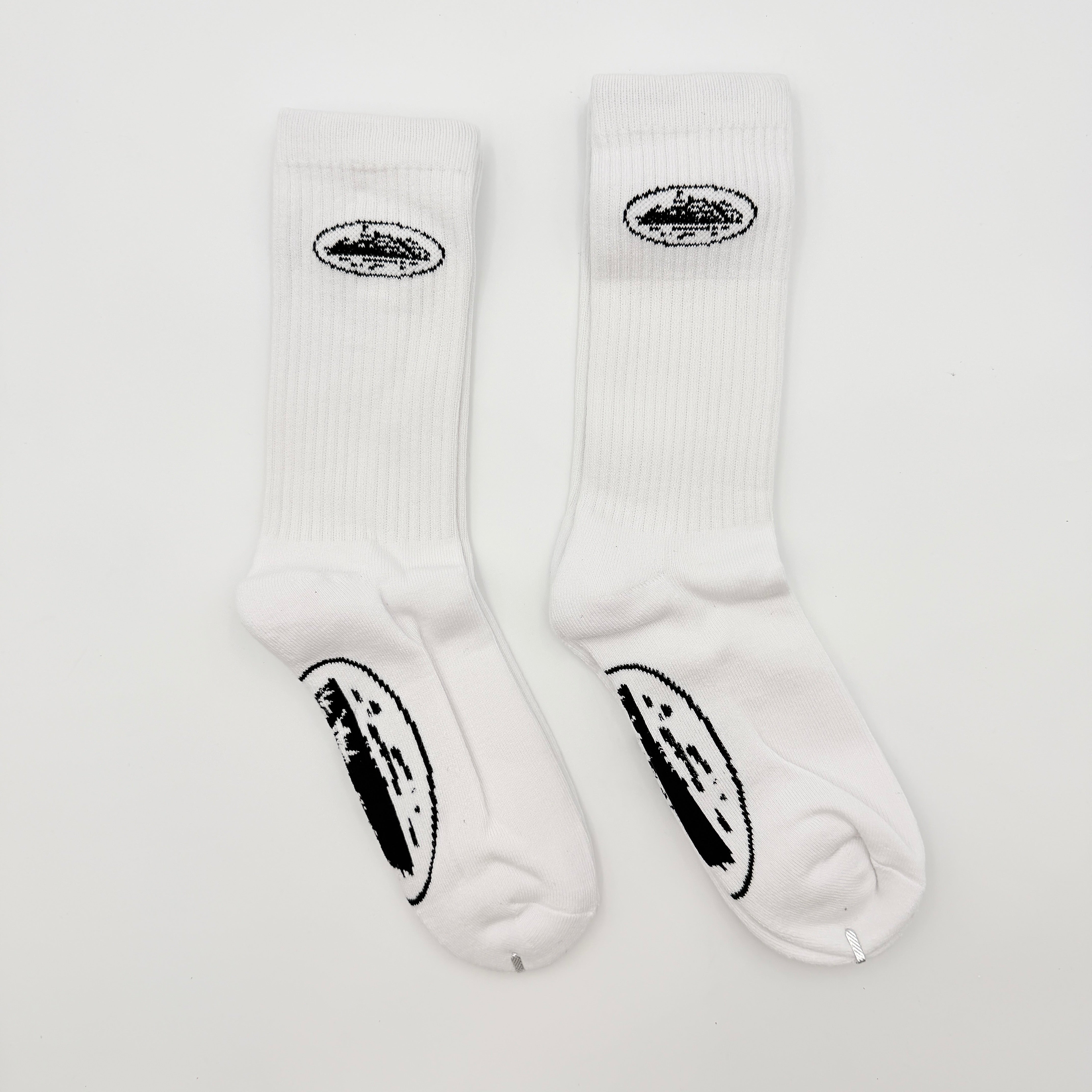 A pair of Corteiz Alcatraz white socks with black logo on the ankle and statement text on the sole.