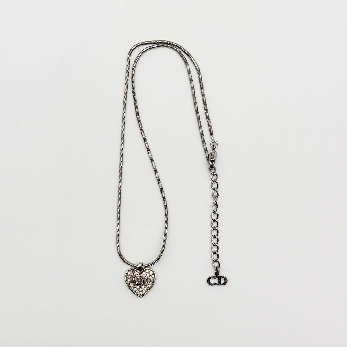 Dior silver necklace with a rhinestone heart pendant and Dior logo, laid flat with CD tag visible.