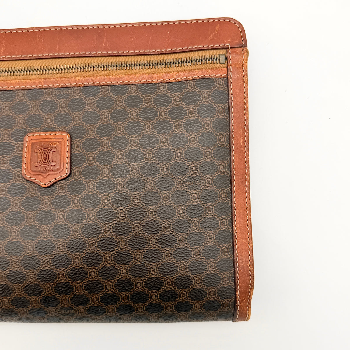 Celine Triomphe Macadam clutch bag in brown canvas with tan leather trim and gold hardware, shown with wrist strap.