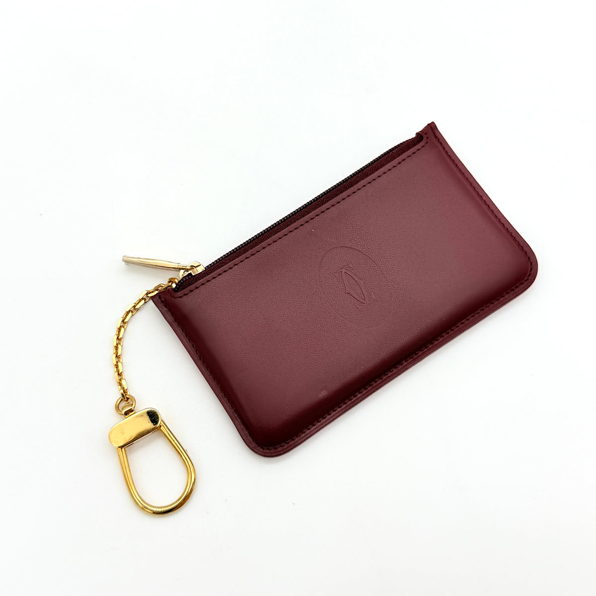 Cartier Must de Cartier burgundy leather coin purse with gold chain key holder and embossed logo, photographed on white.