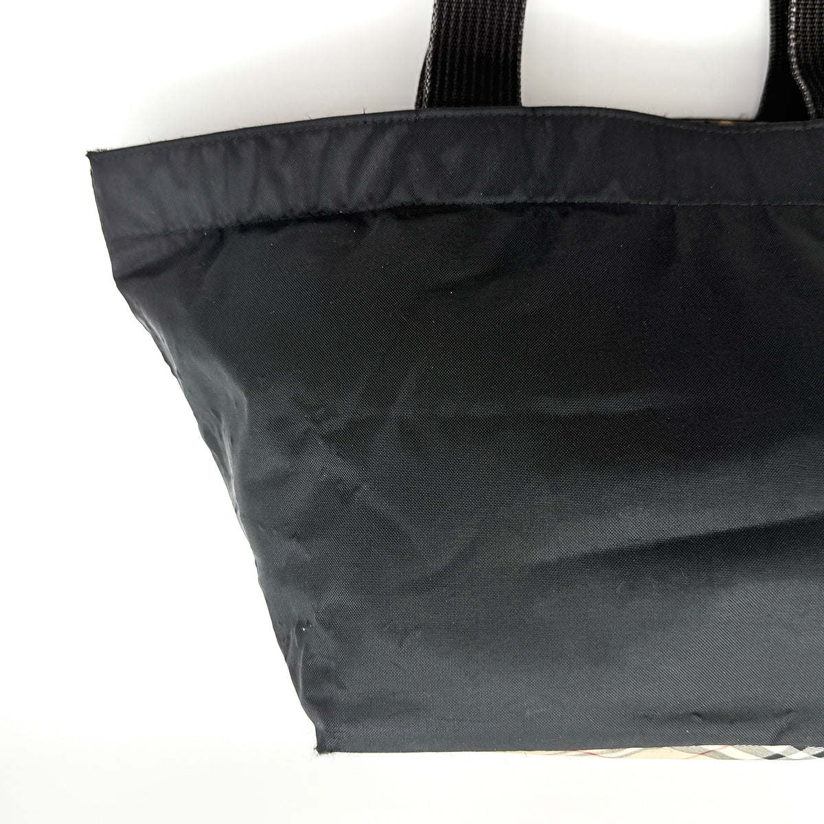 Burberry Blue Label Nova Check tote bag in black nylon with beige checked base and webbed handles, shown on white background.