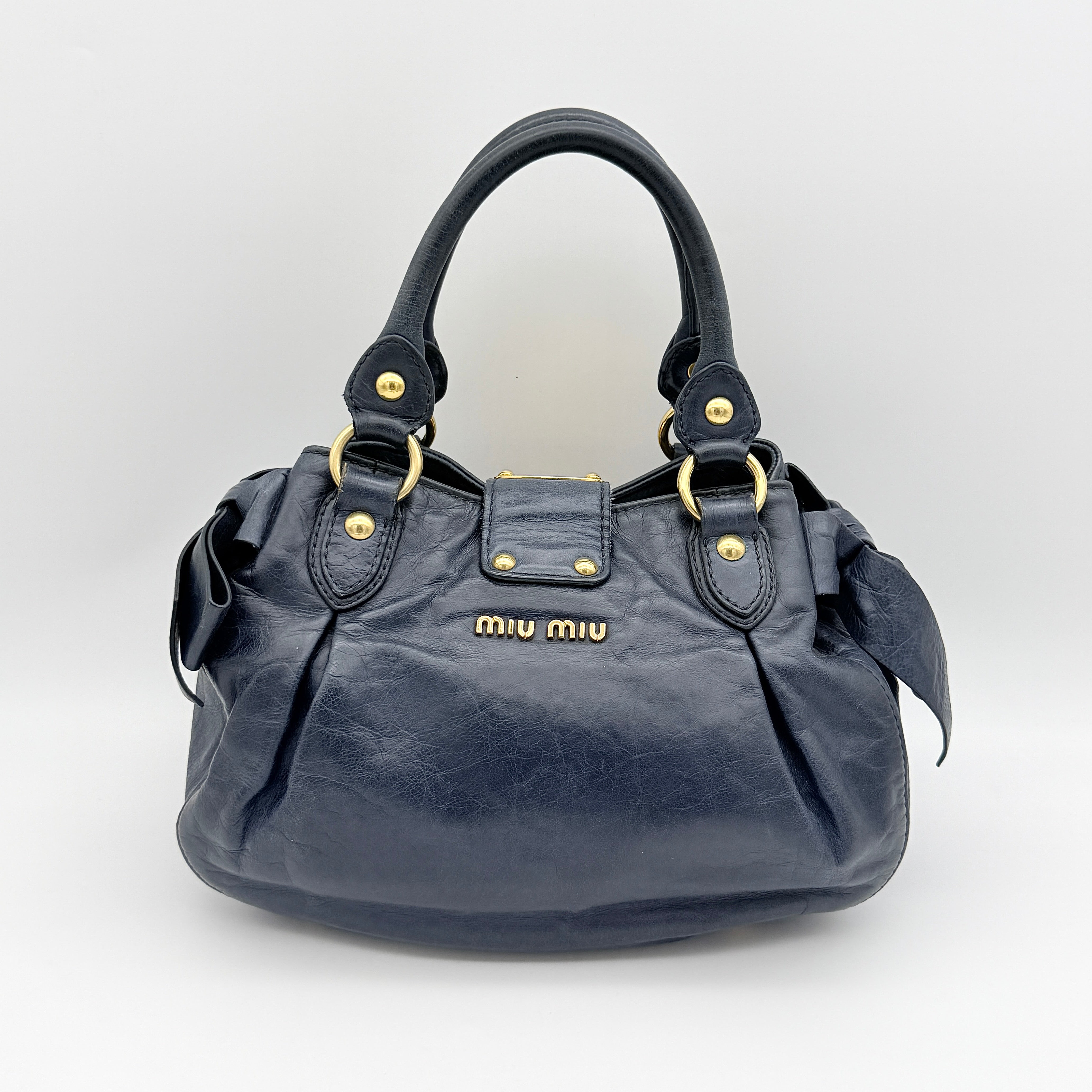Miu Miu navy blue Vitello Lux Bow Satchel with gold-tone hardware, detachable strap, and dust bag.