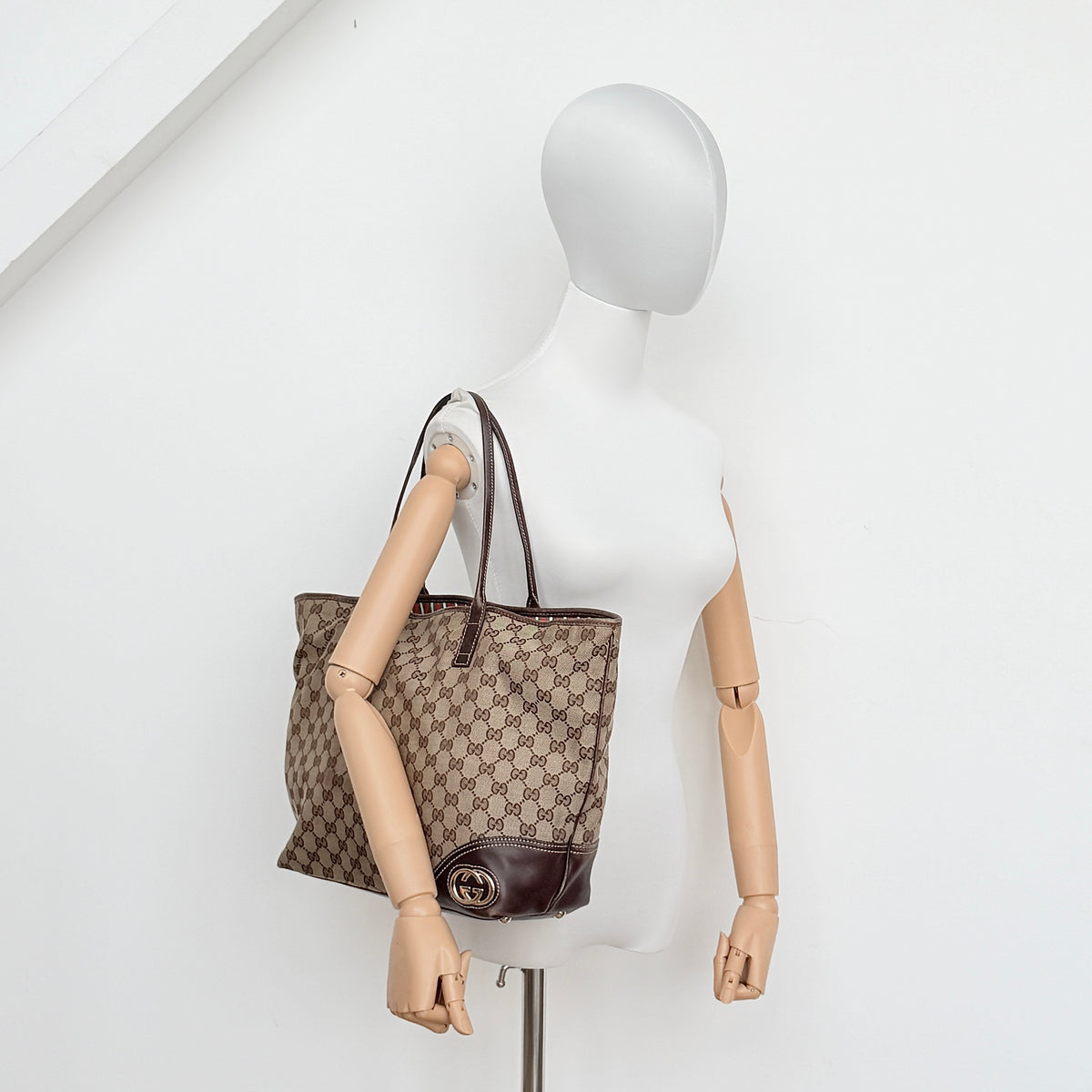 Gucci GG Monogram New Britt Tote Bag in beige and brown canvas with leather trim and gold-tone logo, presented against a white backdrop.