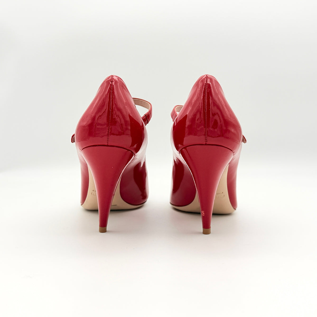 A pair of red patent leather Miu Miu Mary Jane heels with adjustable buckle straps and high heels, displayed against a white background.