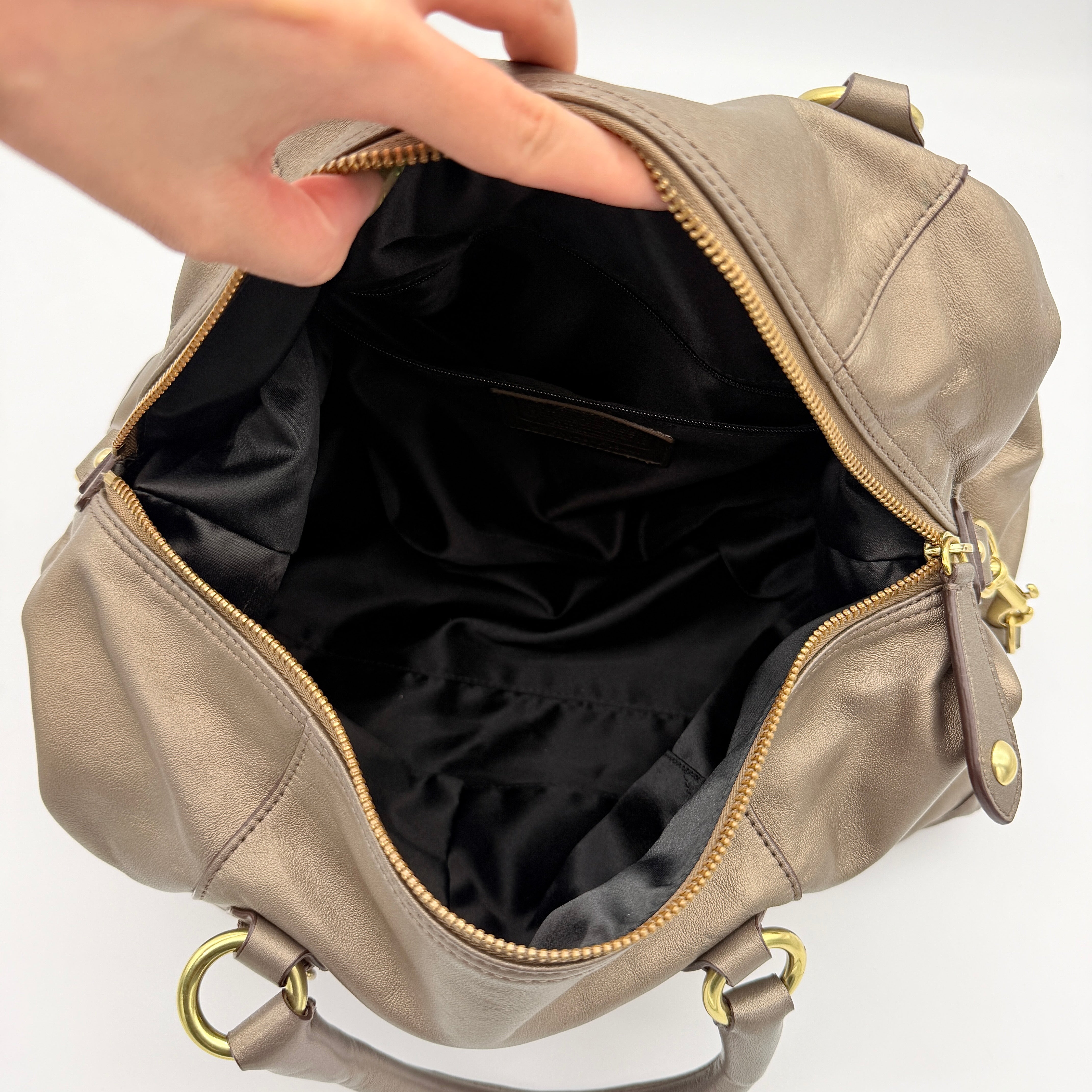 Coach Ashley satchel handbag in metallic bronze leather with gold-tone hardware and detachable shoulder strap, shown against a white backdrop.