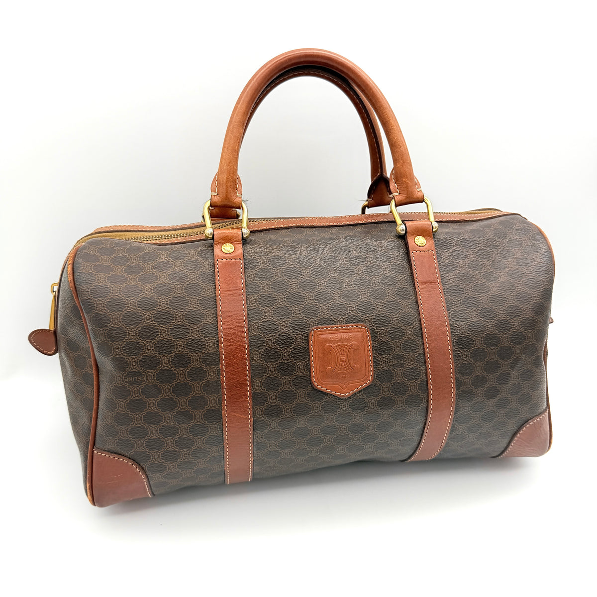 Celine Macadam Triomphe Boston Bag in brown coated canvas with tan leather and gold-tone hardware, shown against a white background.