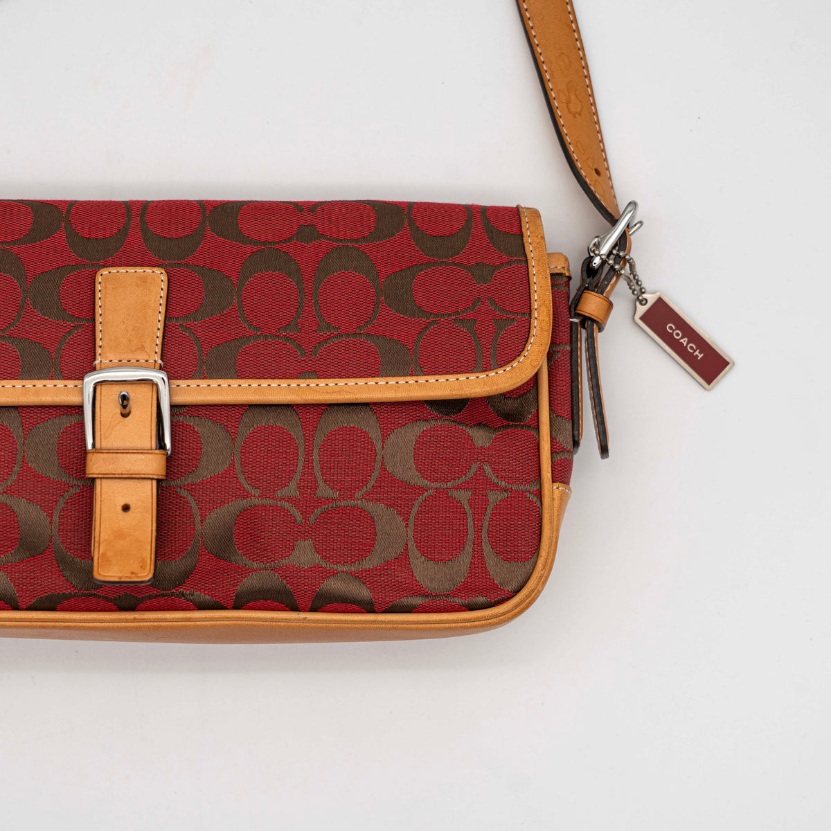 Coach Signature Soho Buckle Baguette in red and tan canvas with leather trim and a silver buckle, shown on a white background.