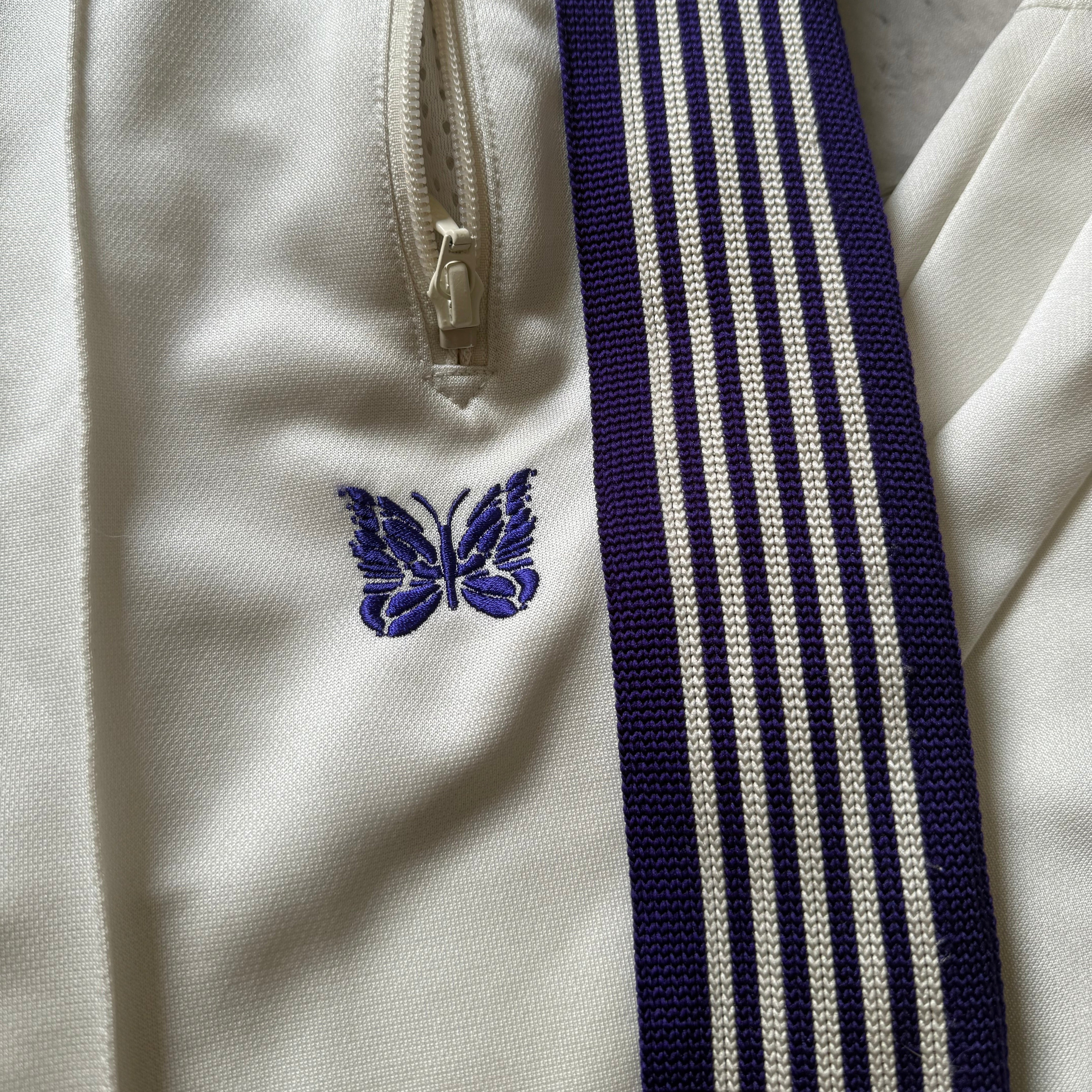 Needles Track Pants White and Purple, featuring striped taping and embroidered butterfly logo with zippered pockets.