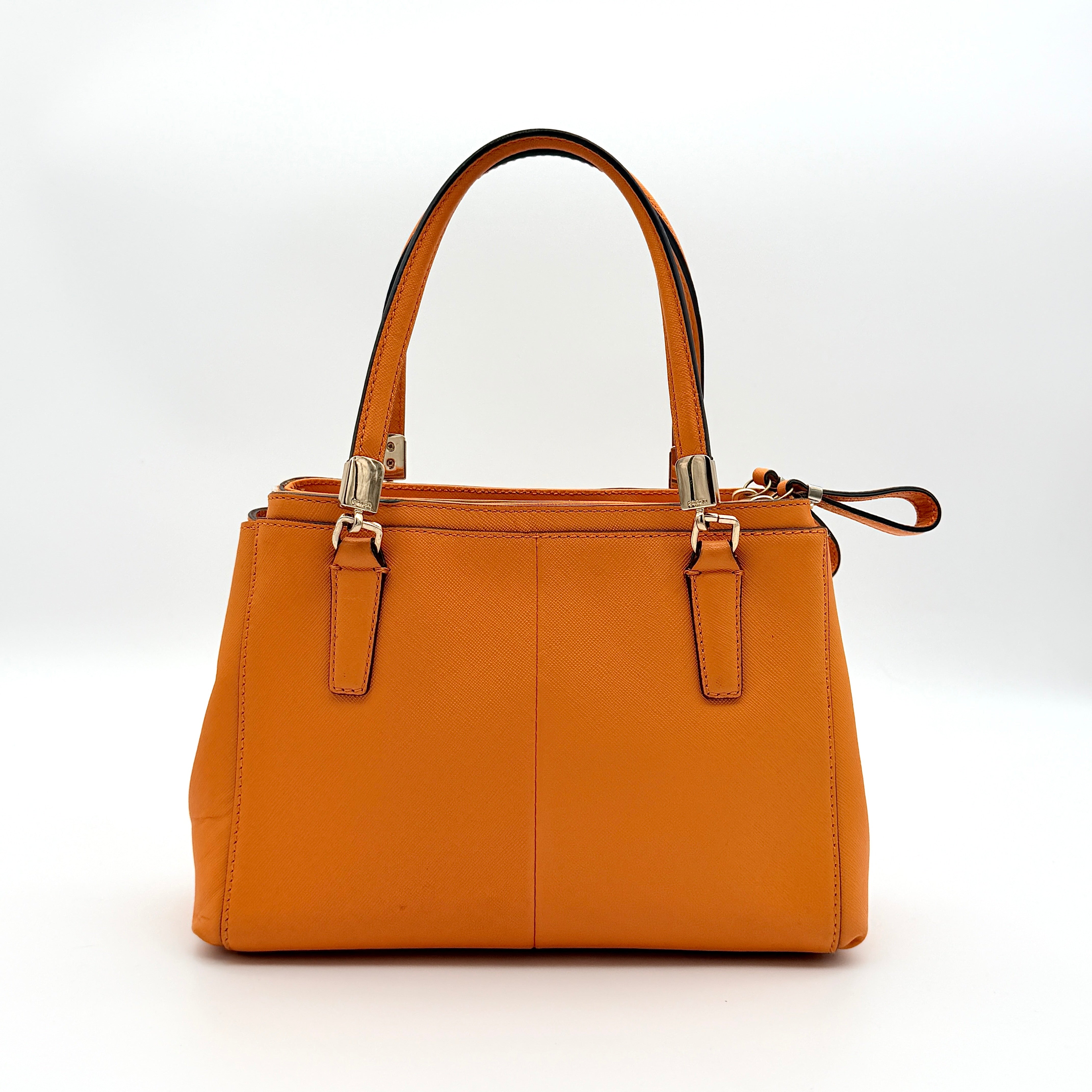 Coach Christie Carryall handbag in orange leather with gold hardware and structured handles, photographed on a white background.