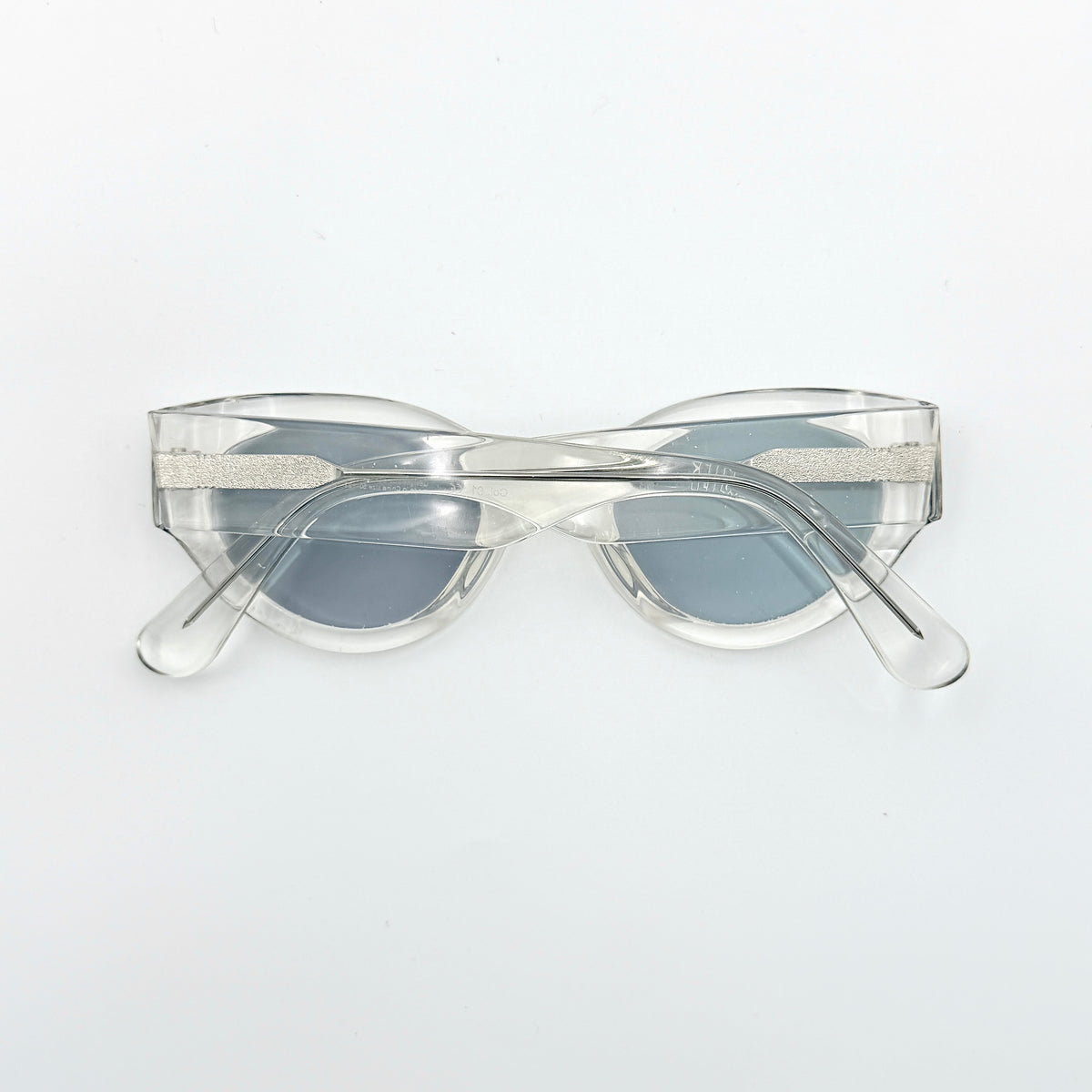 Gentle Monster Tazi transparent sunglasses with grey lenses and clear acetate frame, softly styled alongside the branded case.