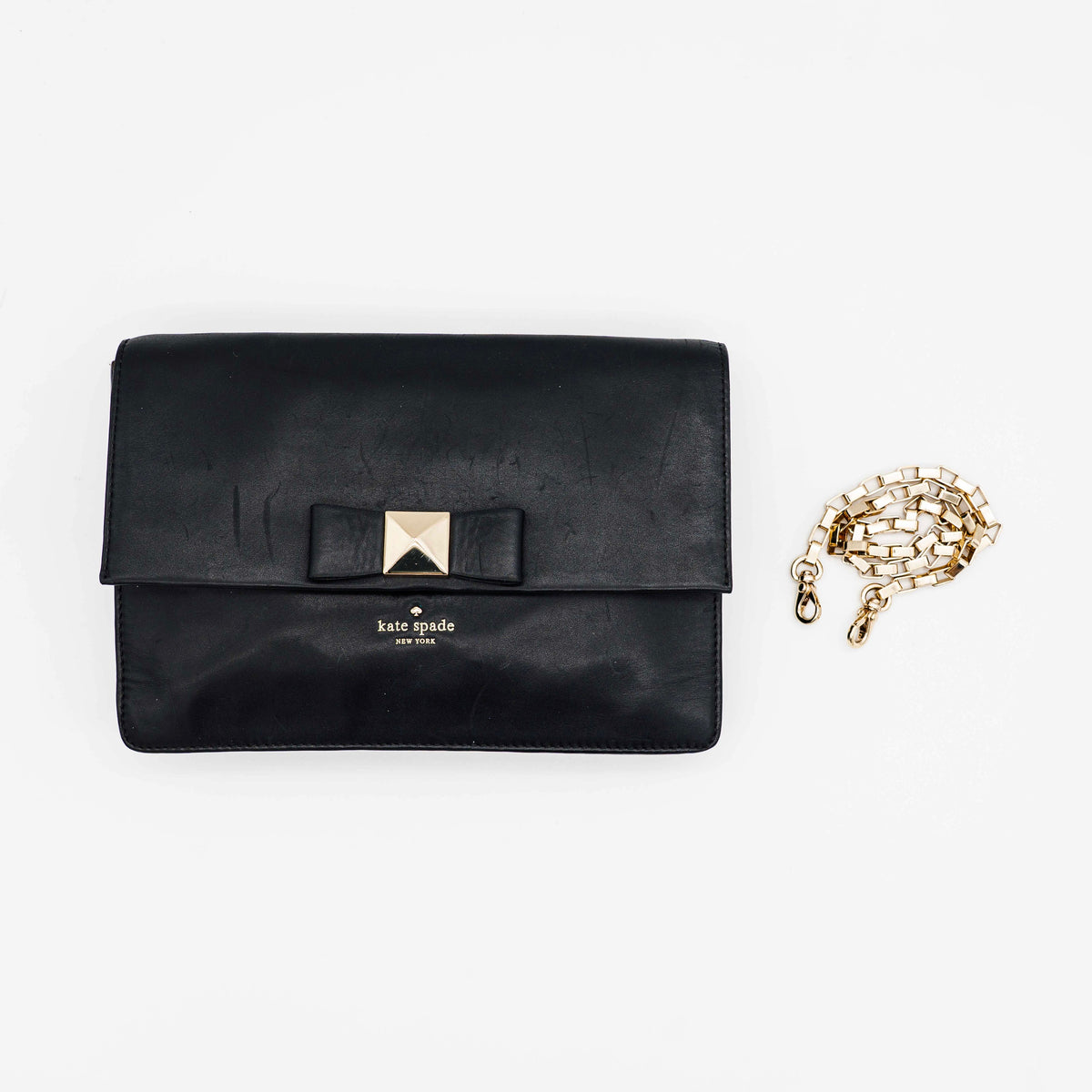 Kate Spade New York black leather shoulder bag with gold chain strap and bow detail, displayed against a white background.