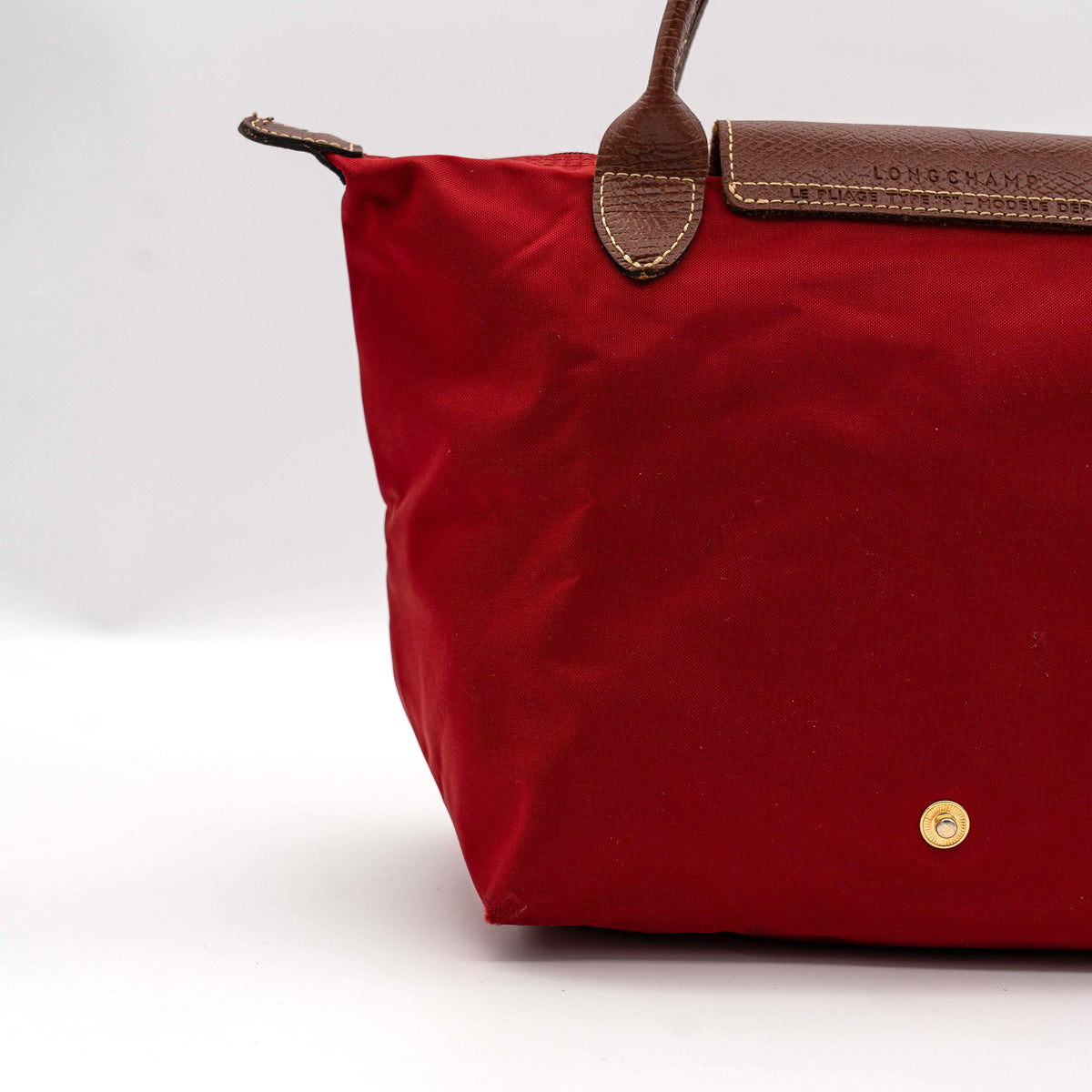 Longchamp Le Pliage handbag in red nylon with brown leather handles and gold-tone accents, photographed on a white background.