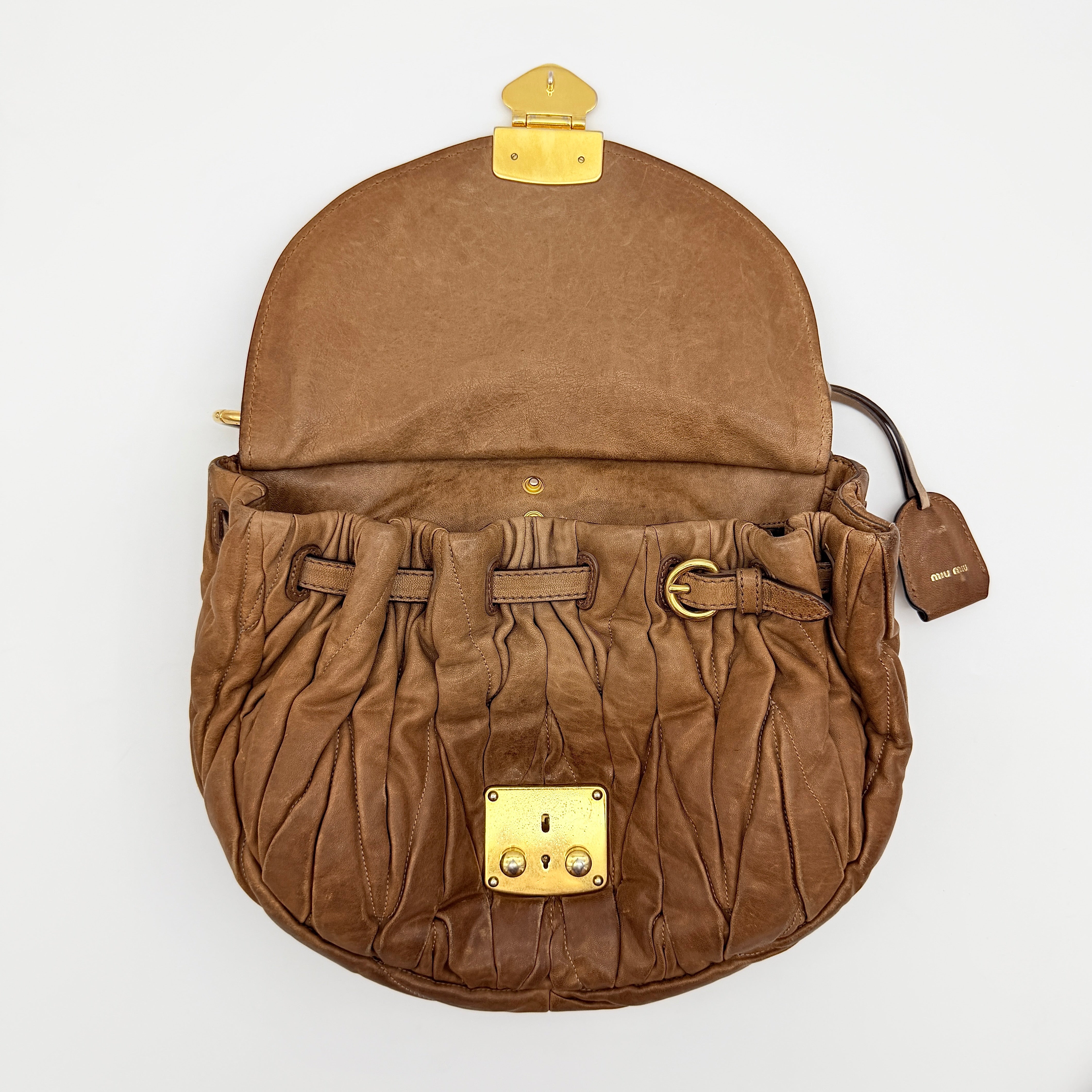 Miu Miu brown Matelasse Coffer Hobo bag with gold hardware, detachable strap, and dust bag displayed on a flat surface.
