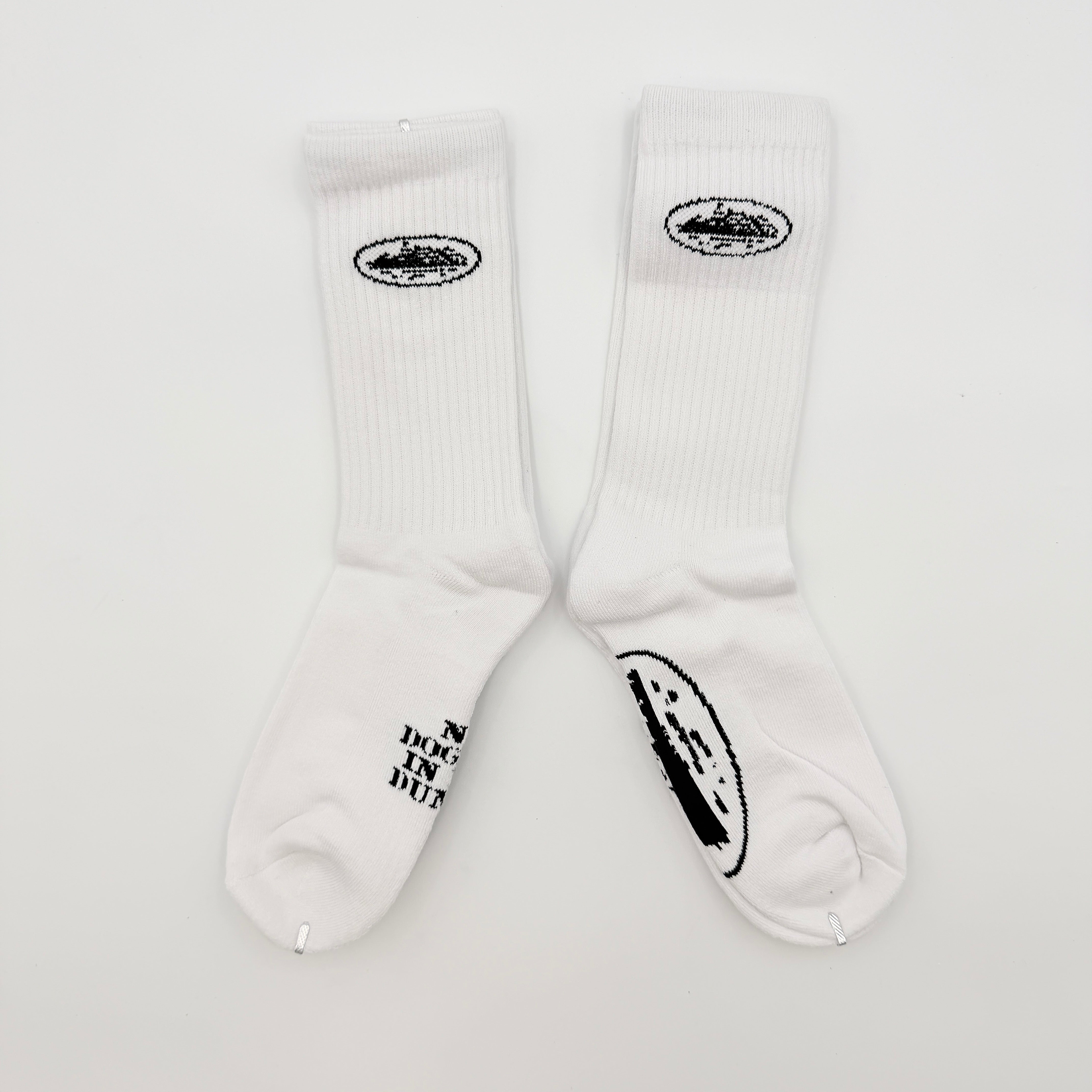 A pair of Corteiz Alcatraz white socks with black logo on the ankle and statement text on the sole.